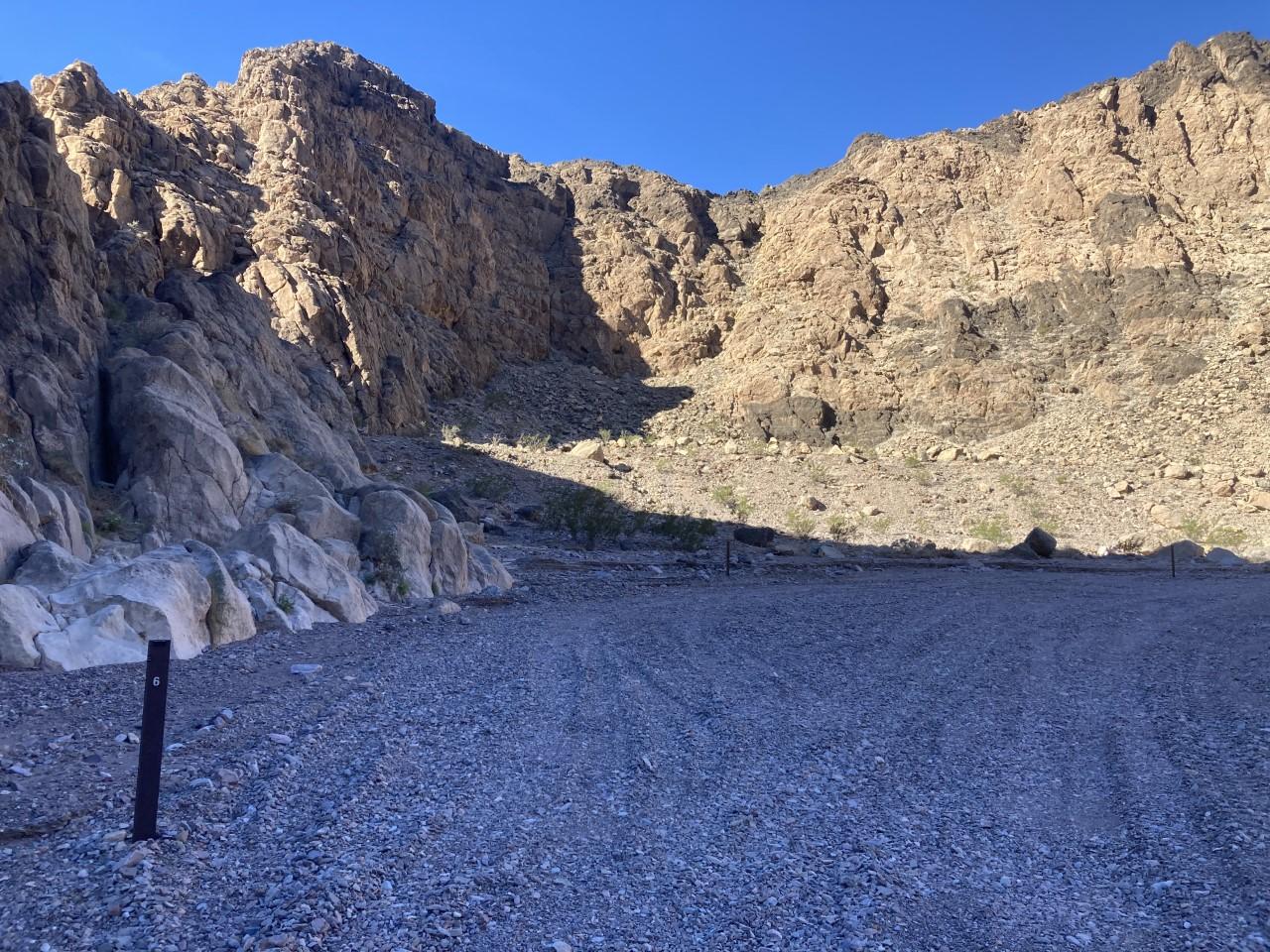 Arid rocky canyon with gravel ground under bright sunlight.
