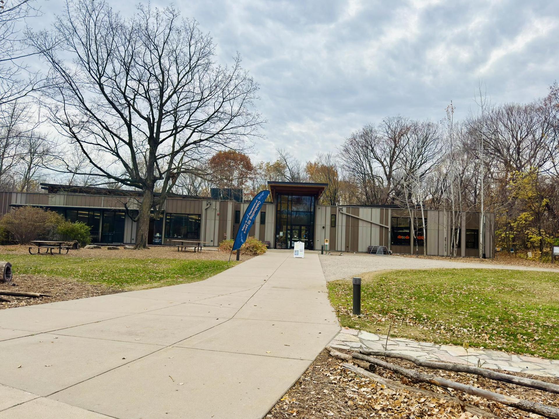 Modern building with glass entrance surrounded by bare trees under a cloudy sky.