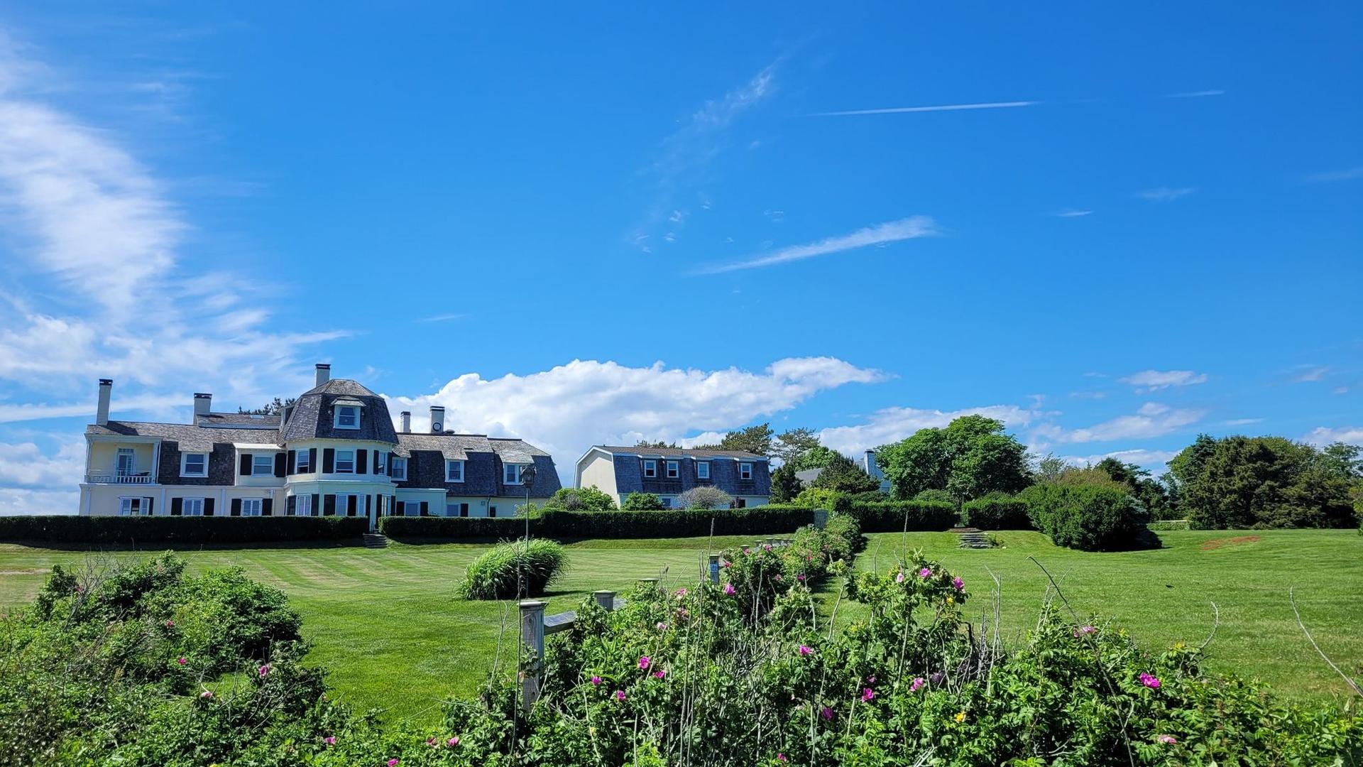 Large white house on a sprawling green lawn under a clear blue sky.