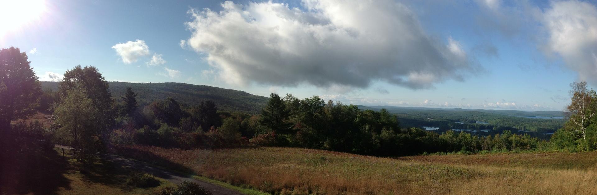 Panoramic view of a sunny, hilly landscape with forests and an open field.