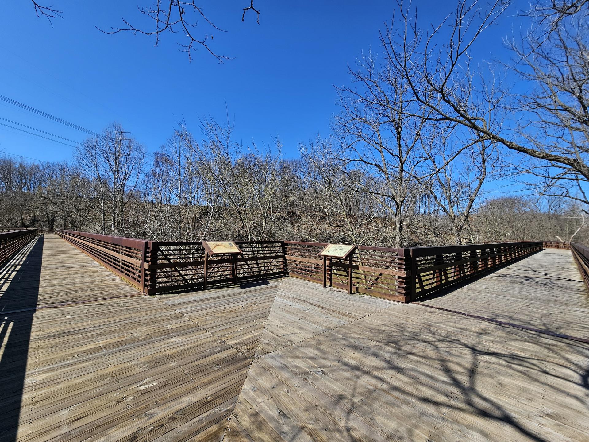 Wooden boardwalk with metal railings splitting, under a clear blue sky.