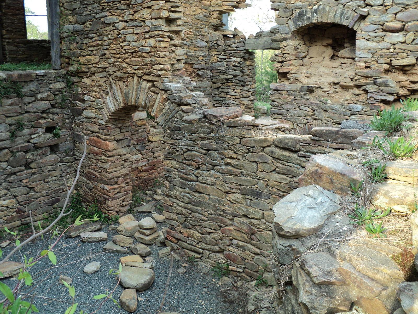 Crumbling stone walls with arched openings and rocky ground in natural light.