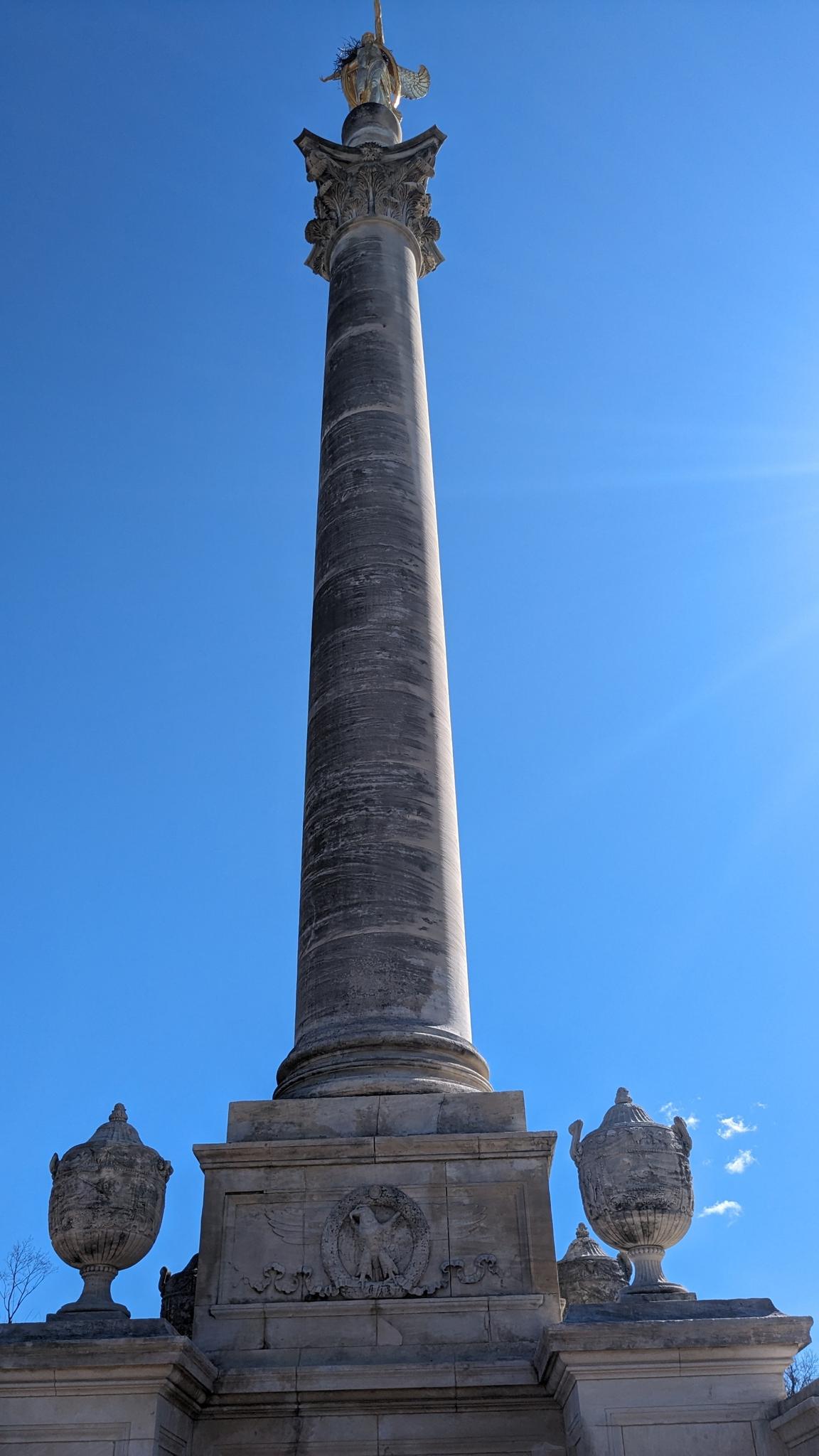 Tall stone column with a statue on top, against a bright blue sky.