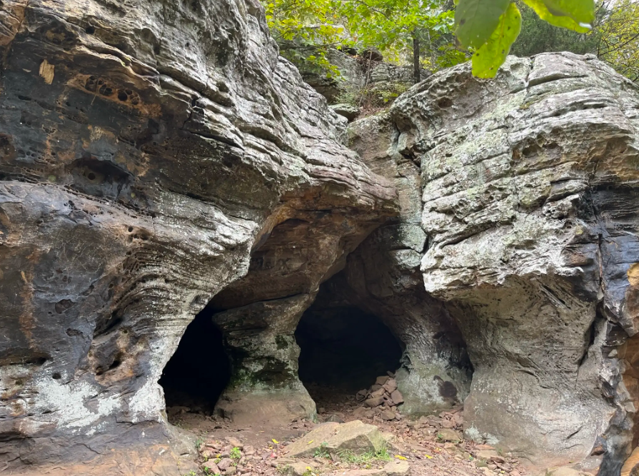 Large, weathered rock formations with dark cave entrances in a natural setting.