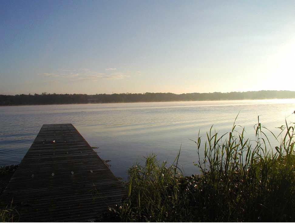A wooden dock extends into calm water at sunrise or sunset.