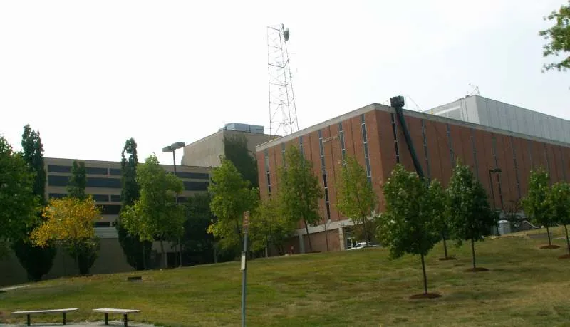 Large brick and concrete buildings behind a grassy hill with young trees. - Wright State Biology Preserve – Wright State Biology Preserve loop from Wright State University