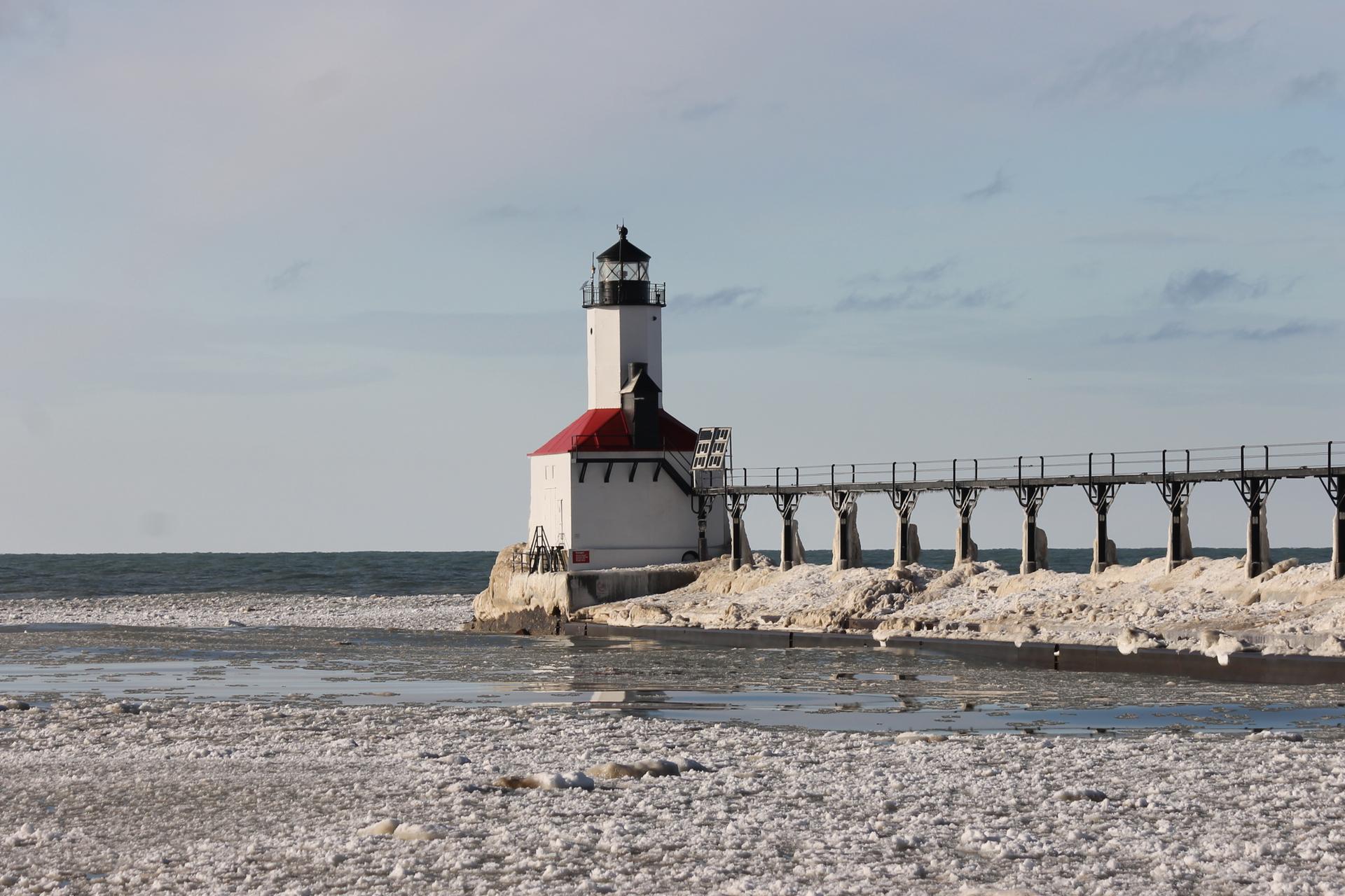 White lighthouse with red roof on a pier over icy water.