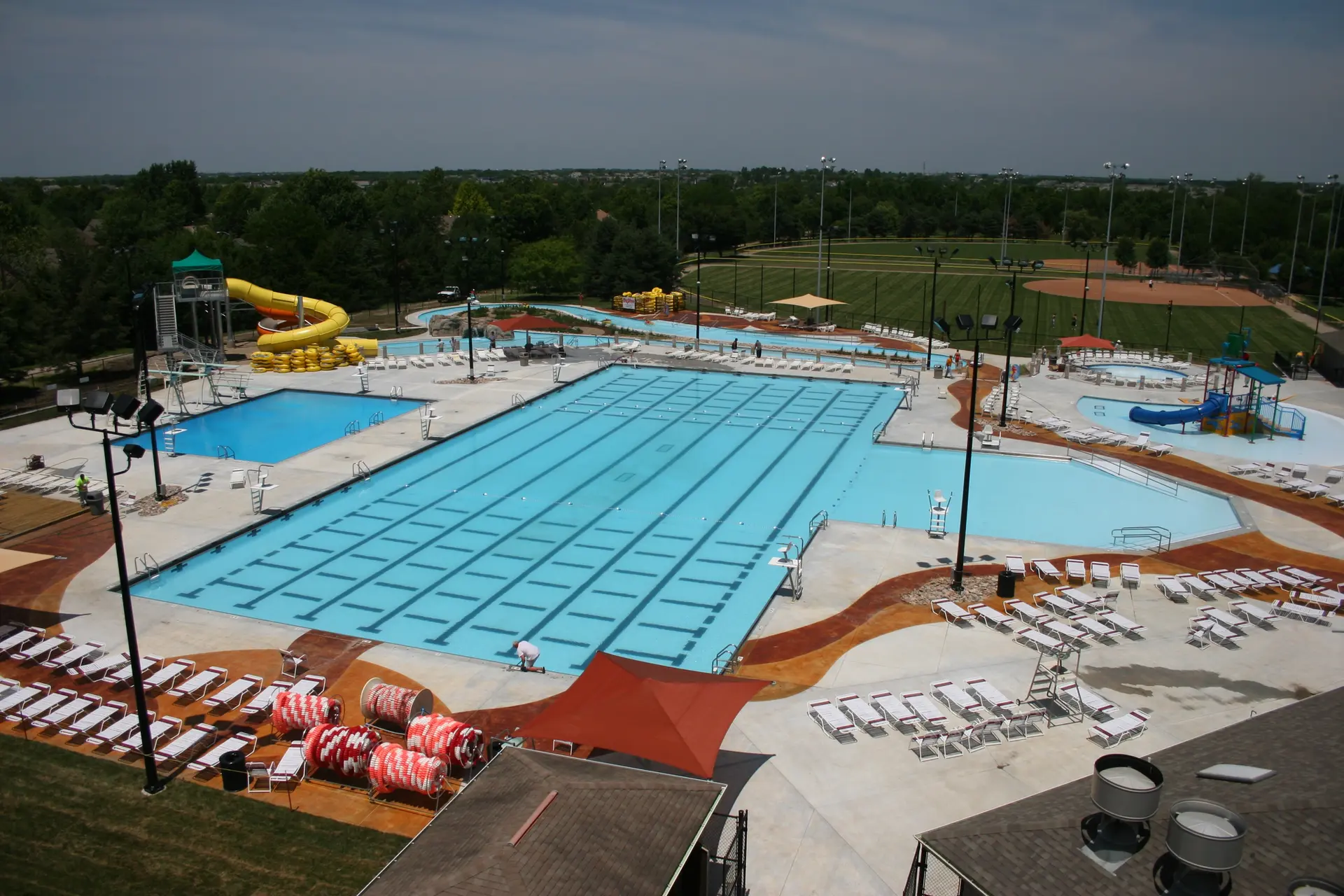 Aerial view of a large, sunny outdoor swimming pool complex with slides and fields.
