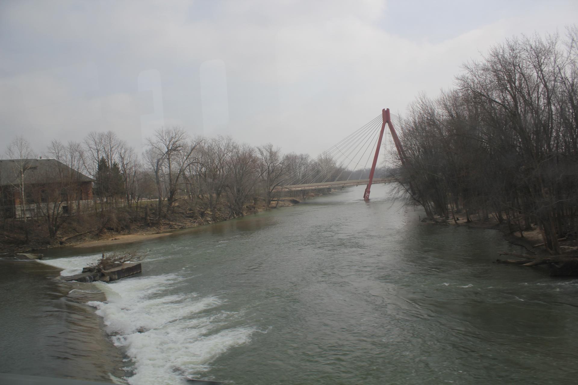 A wide river flows under a red suspension bridge on an overcast day.