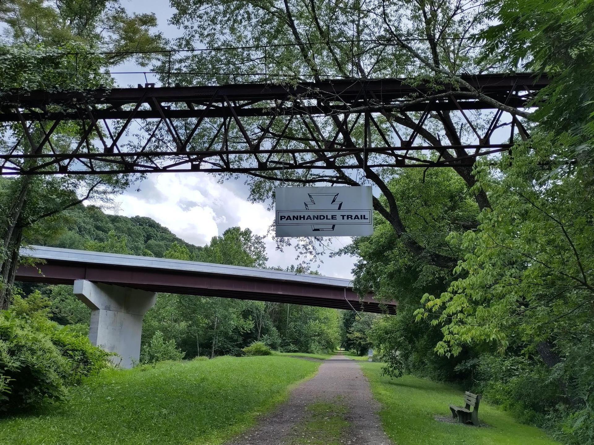 Dirt path under a large metal bridge structure, with another bridge.