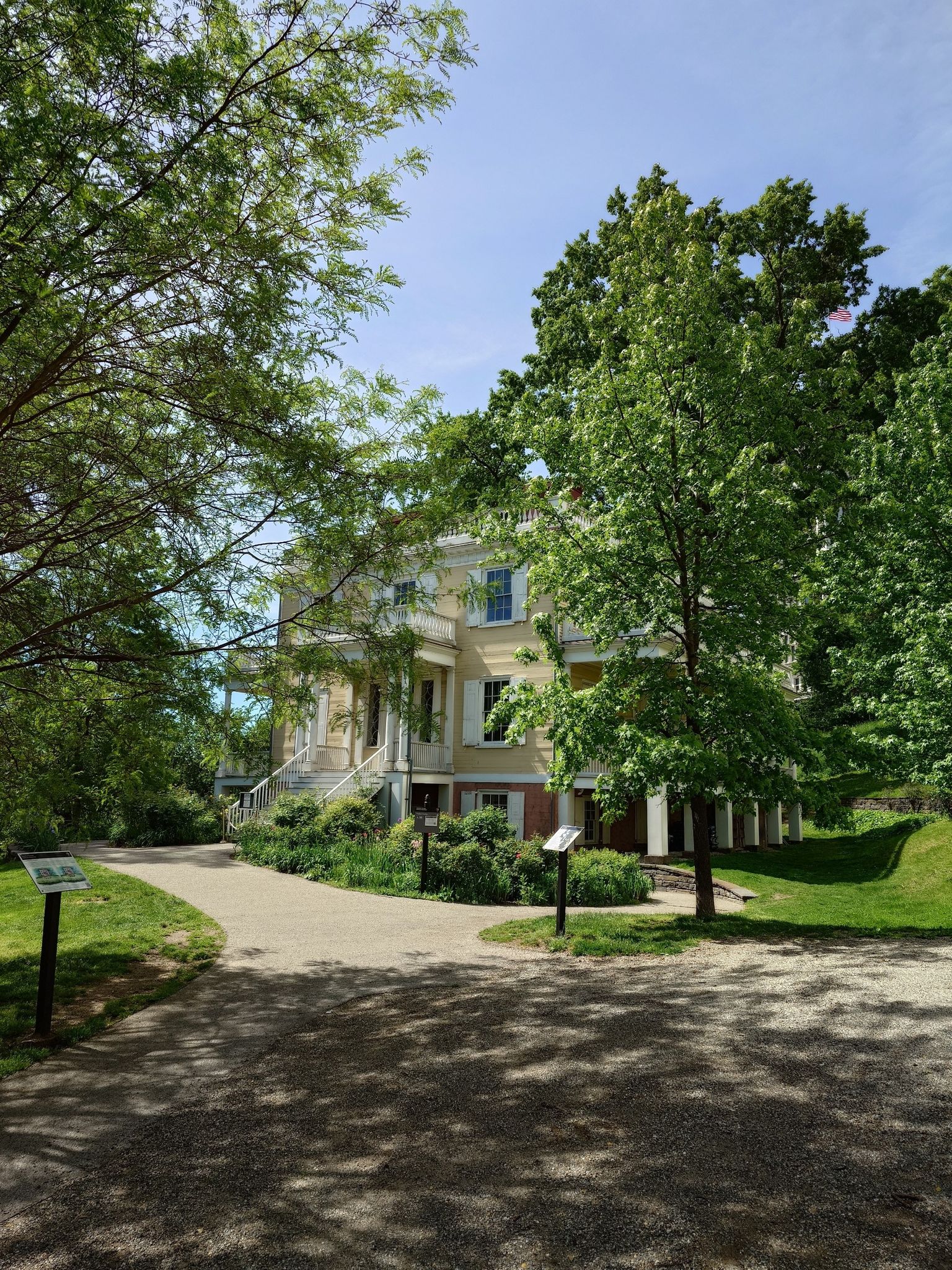 A grand, light-colored building with columns, surrounded by lush green trees on a sunny day. - Saint Nicholas Park Loop