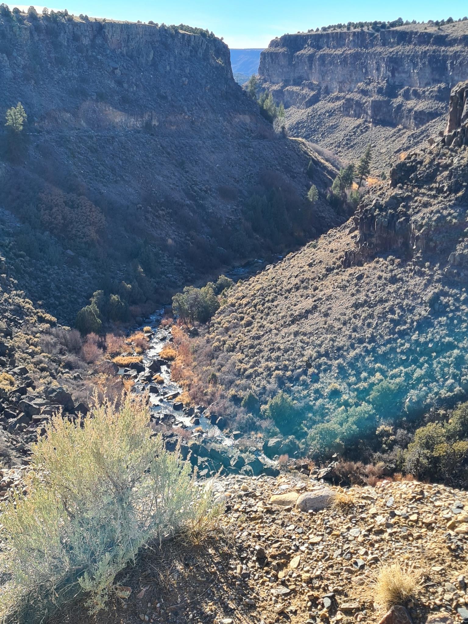 Deep canyon with a winding river, rocky slopes, and sparse vegetation.
