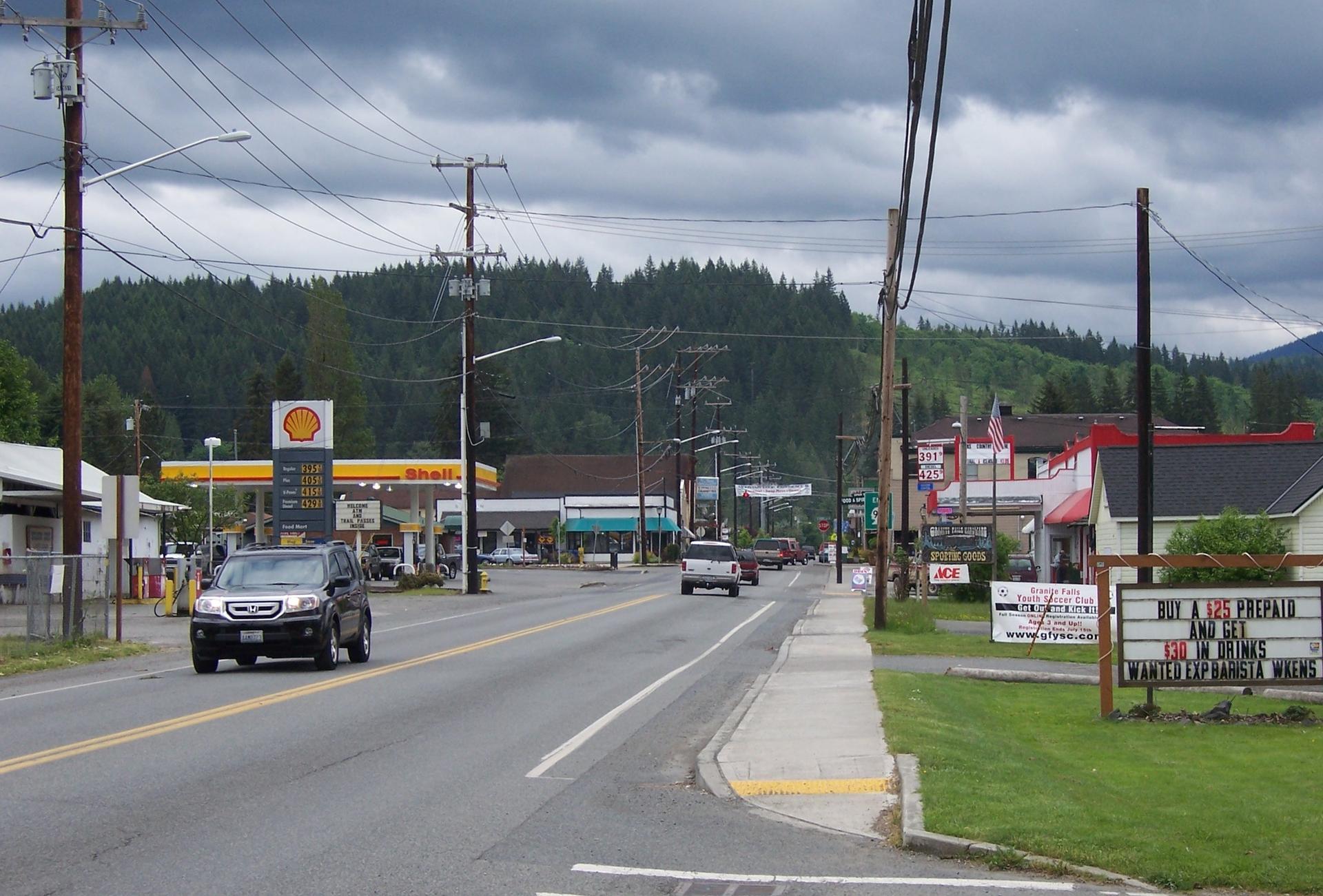 A street with cars, buildings, and power lines under a cloudy sky.