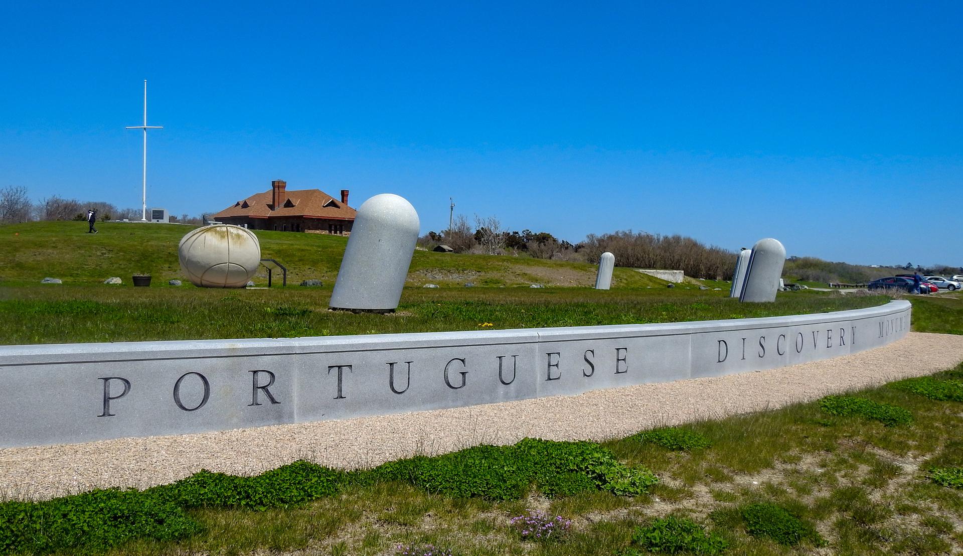 Sunny view of a concrete monument wall on a grassy hill with distant buildings.