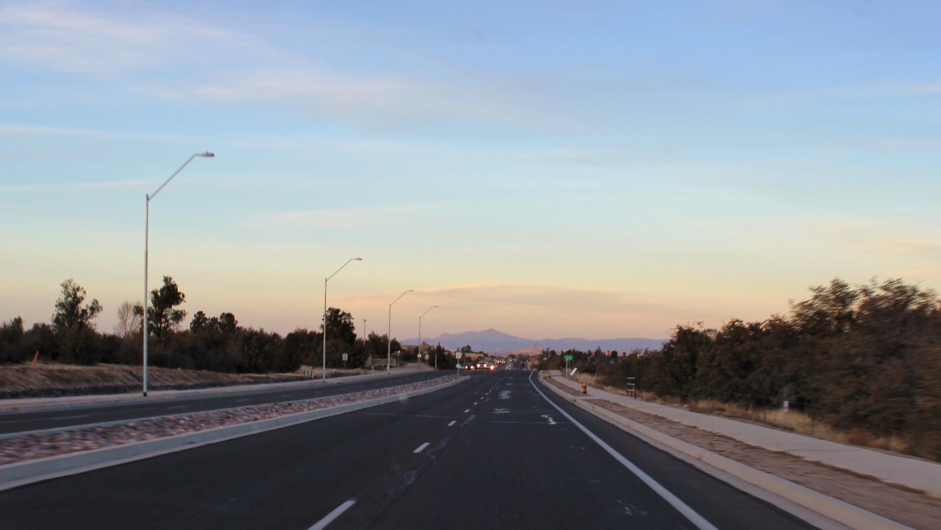 Multi-lane highway at dusk with distant mountains and streetlights.