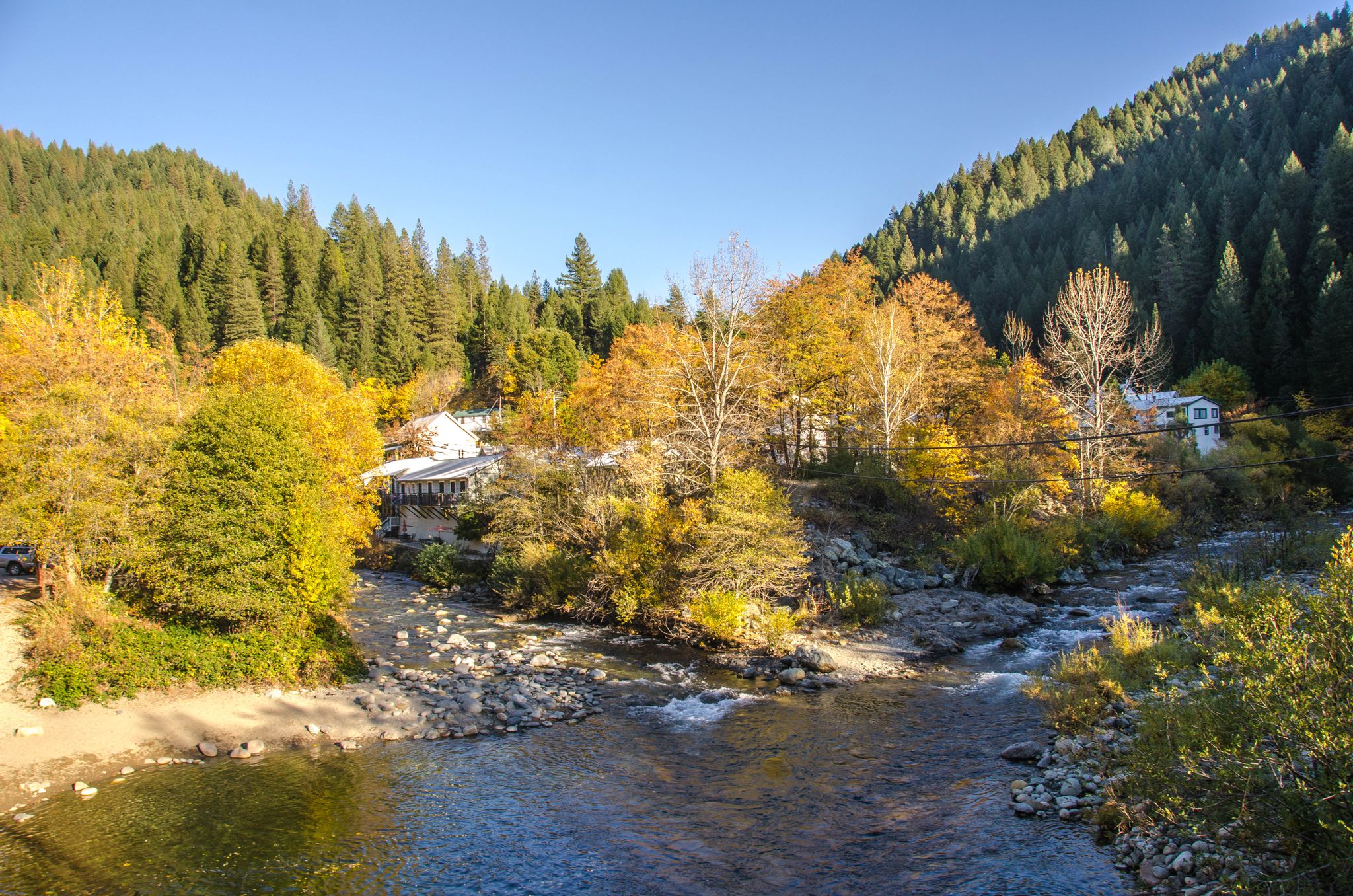 A river flows through a valley with autumn trees and distant houses. - Sierra City & Sierra Buttes Scenic Overlook from Downieville