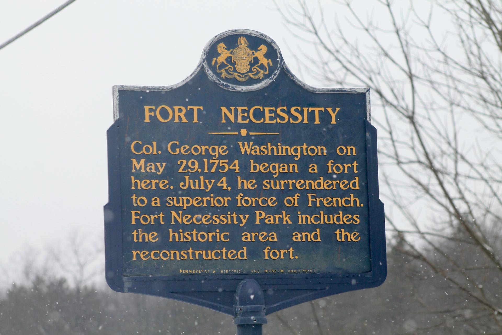 Dark historical marker sign with text against a cloudy, winter sky.