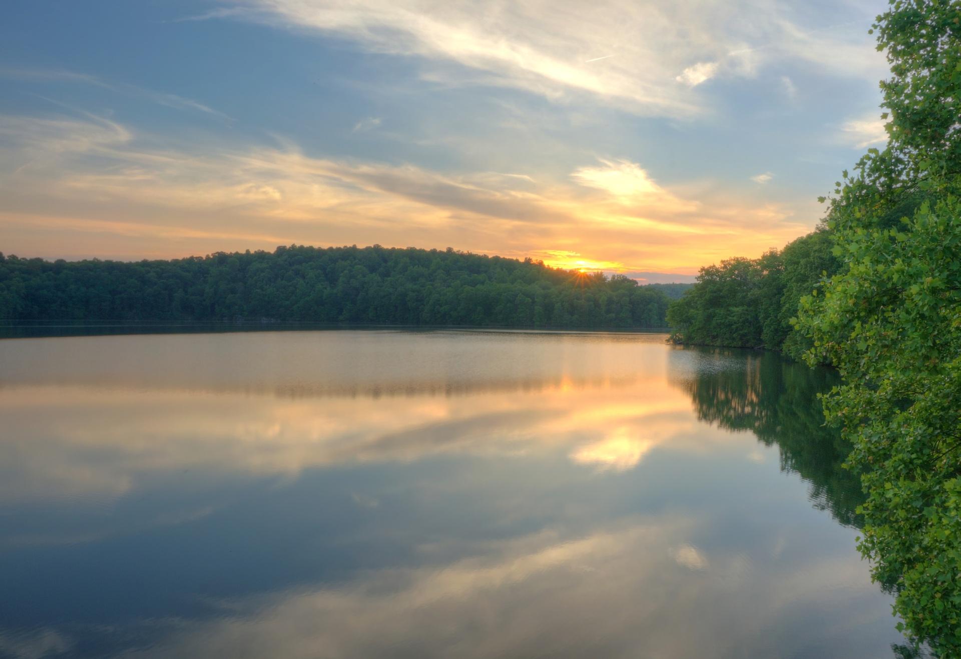 Serene lake reflecting a colorful sunset sky, surrounded by lush green forests.