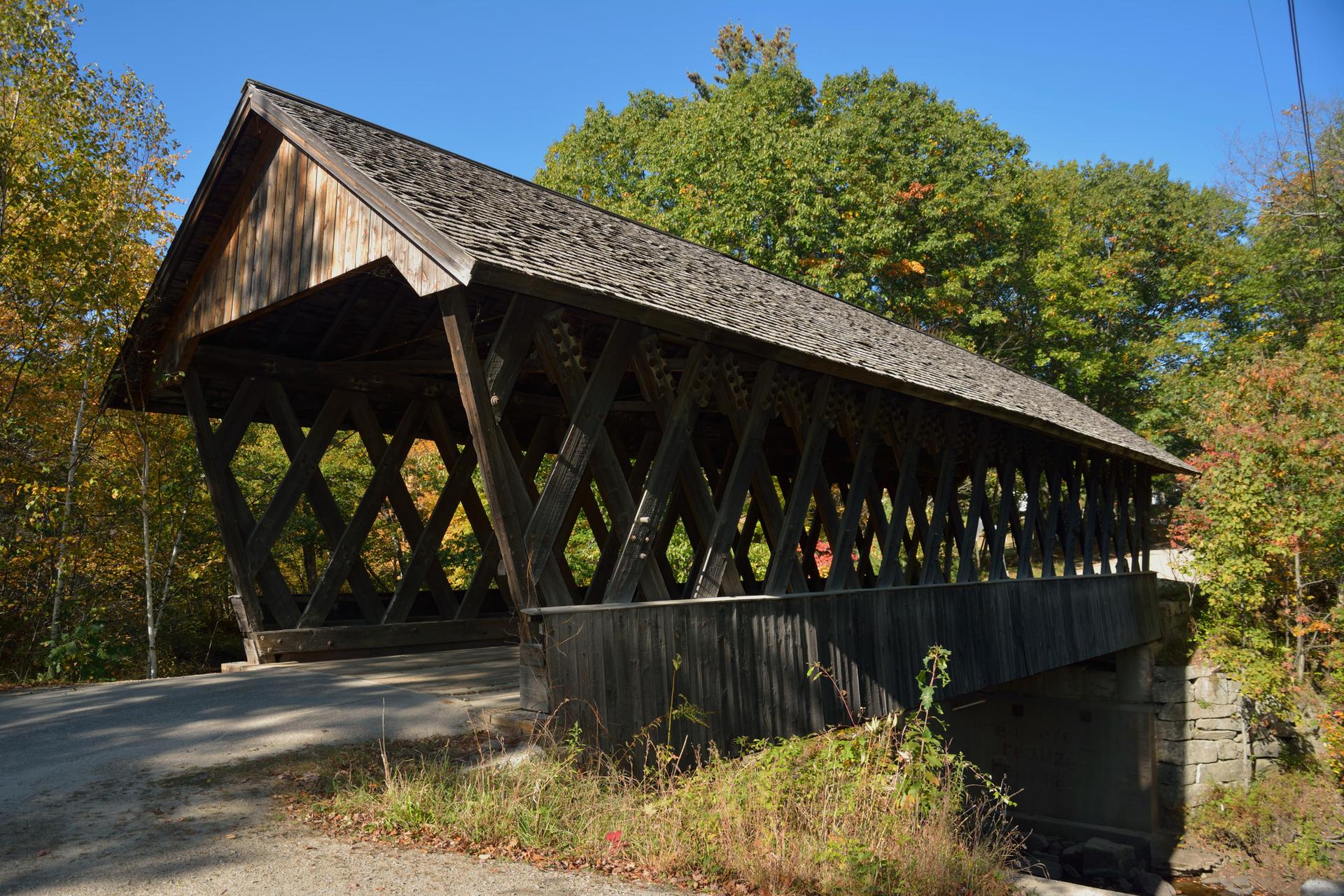 A long wooden covered bridge with lattice sides, surrounded by autumn trees.