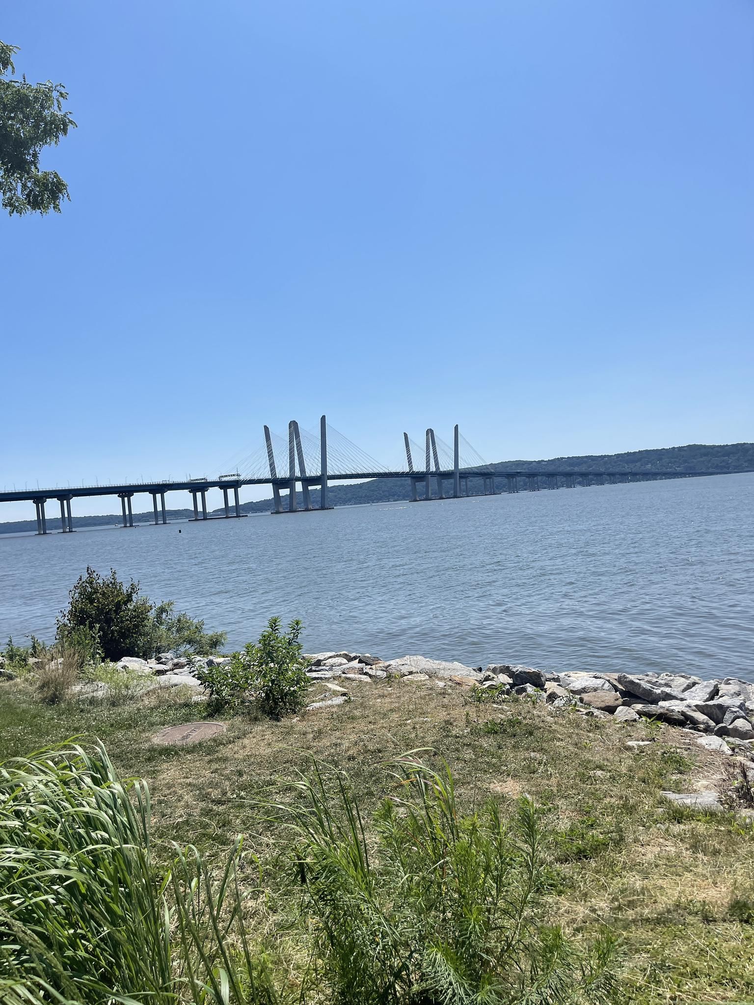Grassy shore by water with a long, distant bridge under clear sky. - Terrytown Main Street – Tarrytown Riverwalk loop from Village of Sleepy Hollow