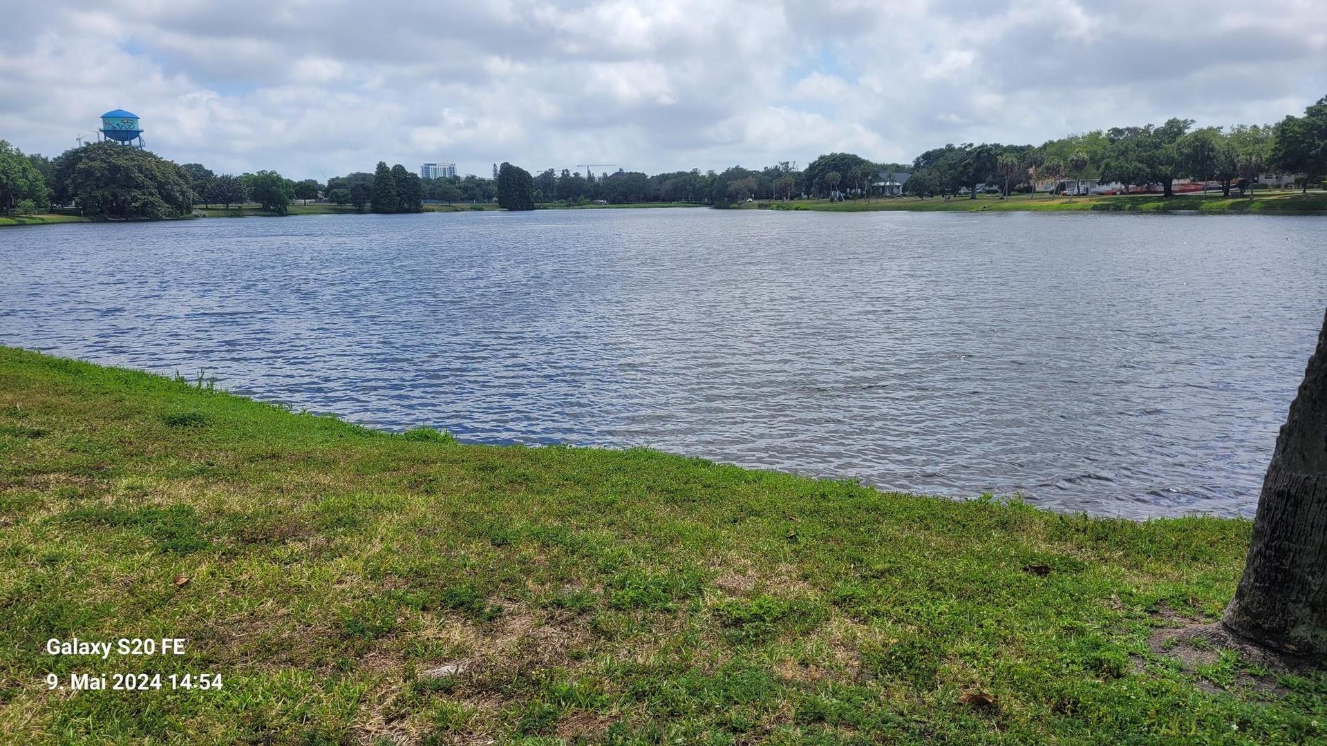 Wide lake with green grassy banks under a cloudy sky, distant water tower.