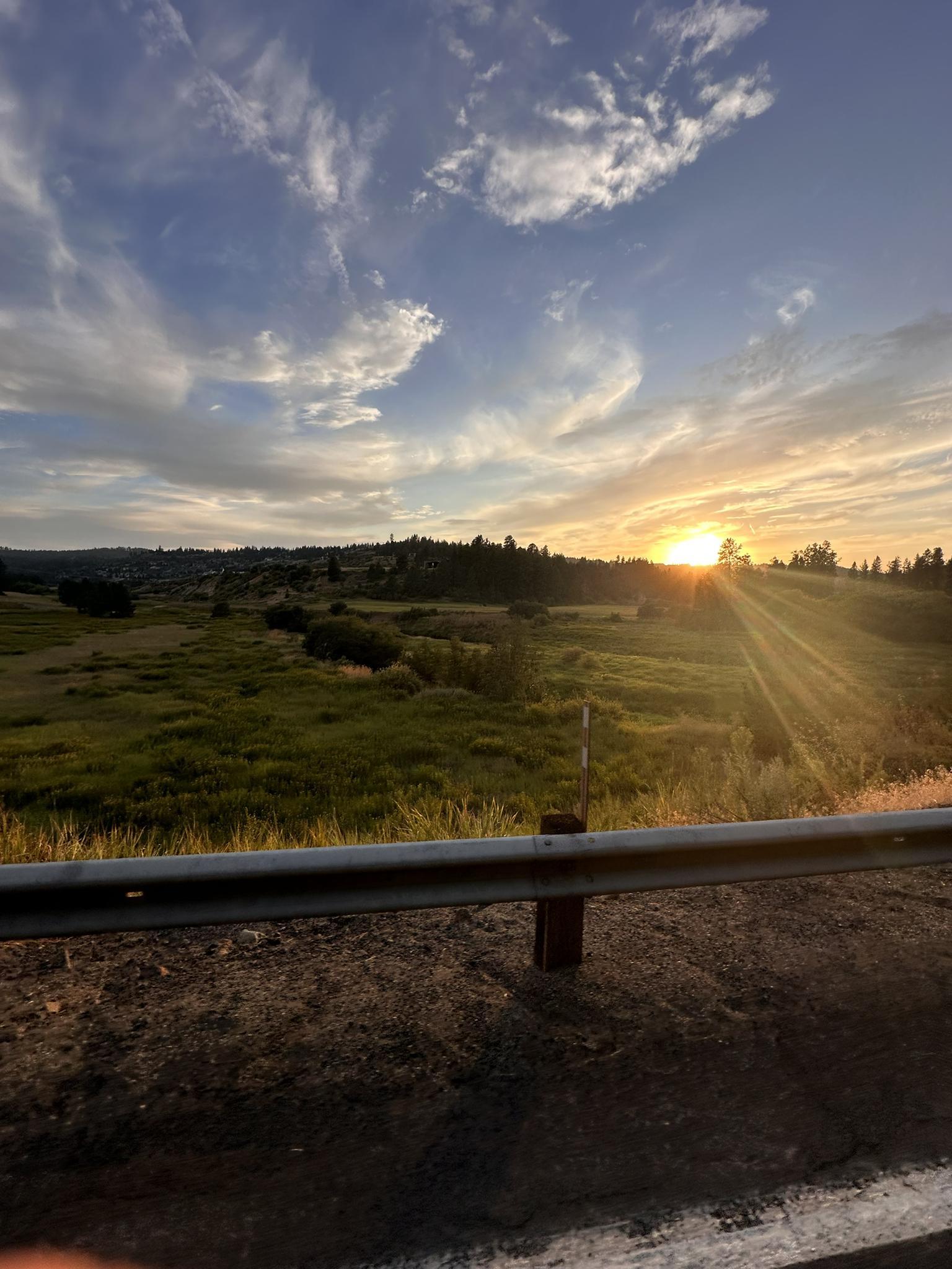 Golden sunset over a green field with sun rays beaming through clouds.