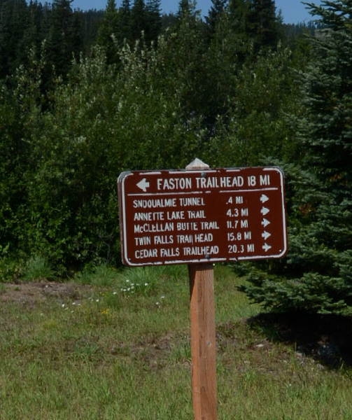 Brown trail sign with white text, indicating various trailheads and distances.