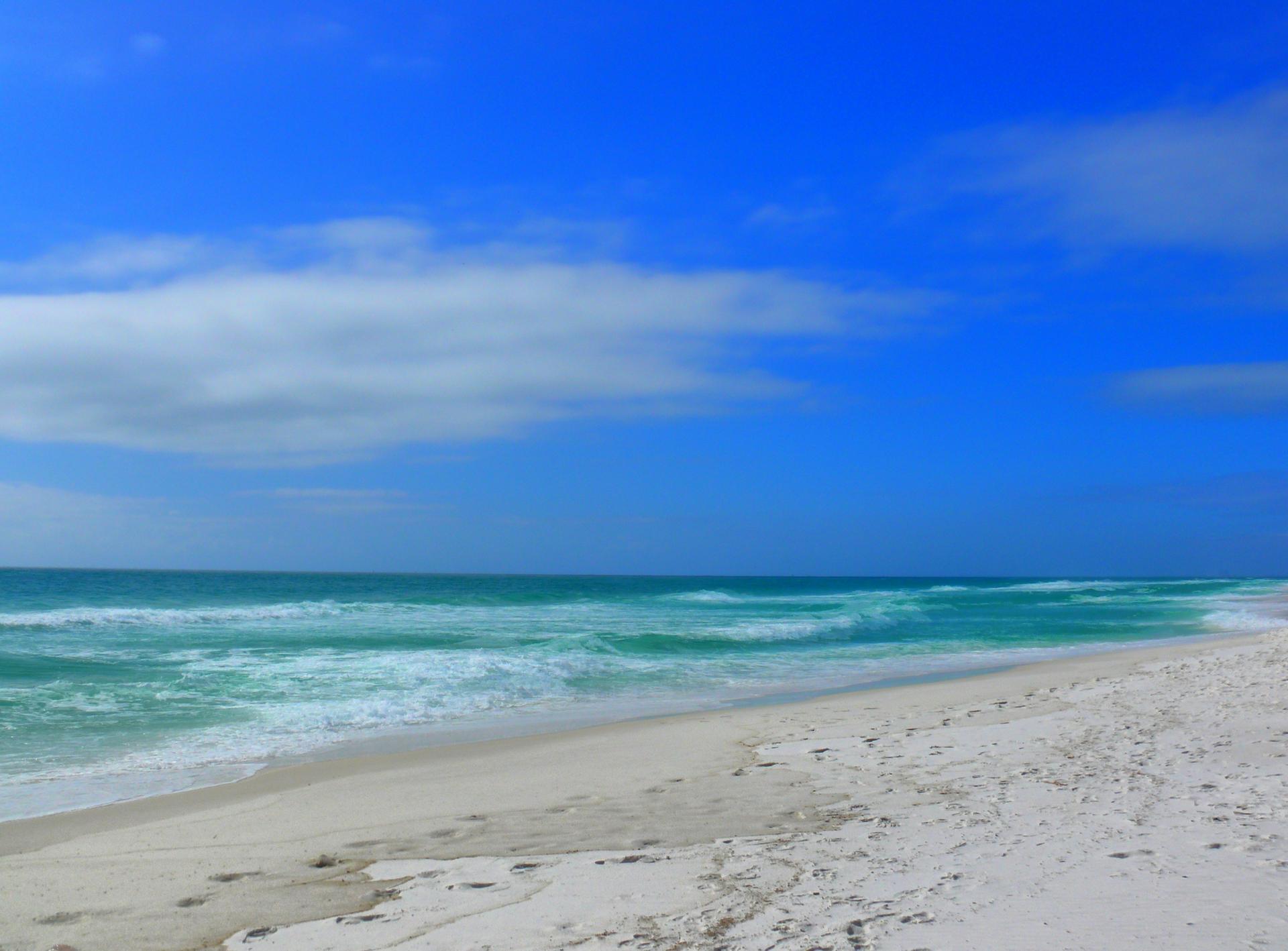 Expansive white sand beach with turquoise waves under a bright blue sky.