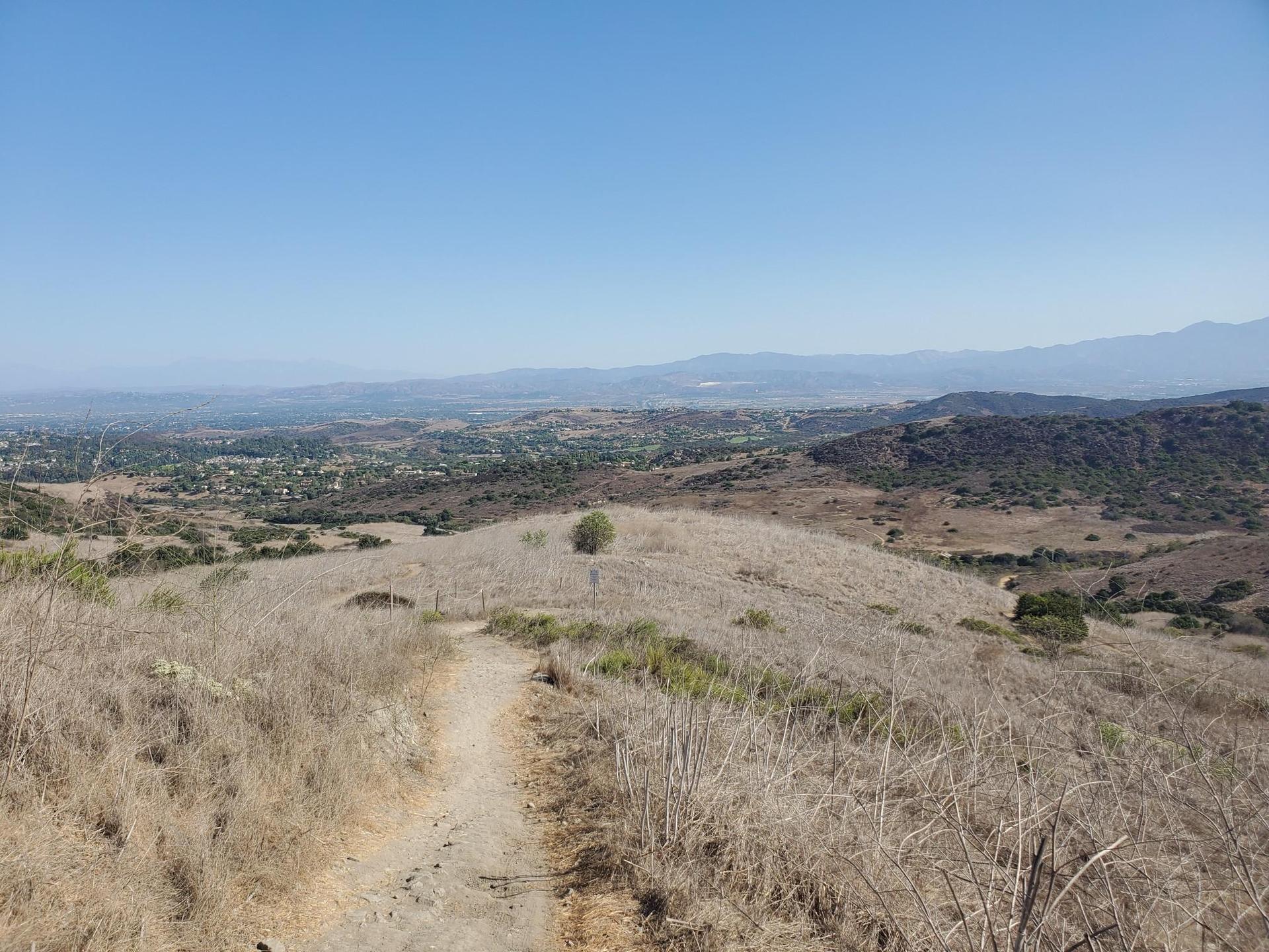 Dirt path on a dry hill overlooking a valley and distant mountains.