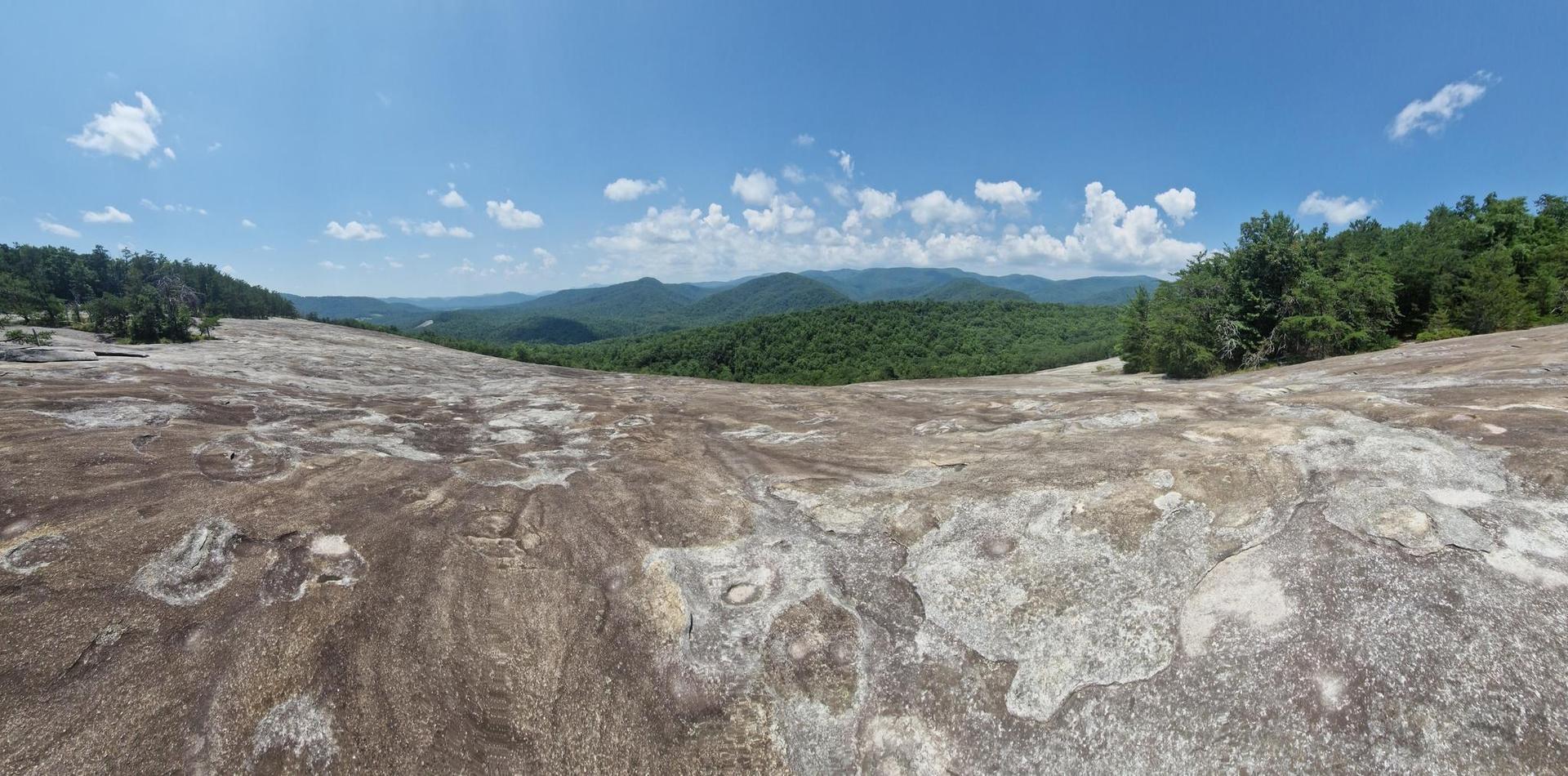 Expansive textured rock surface under a bright blue sky with distant mountains.