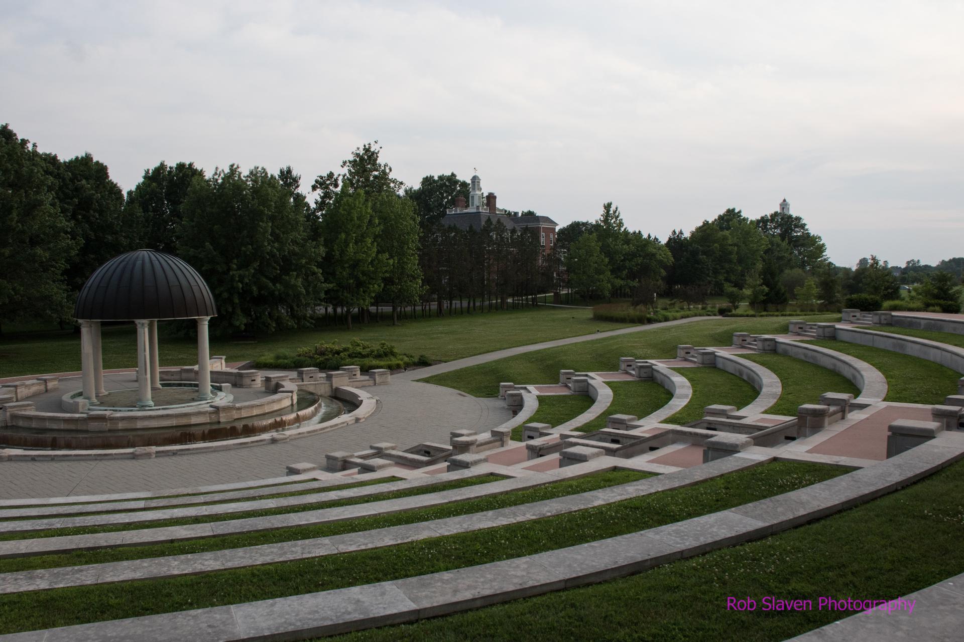 An outdoor amphitheater with a gazebo and grassy seating under an overcast sky.
