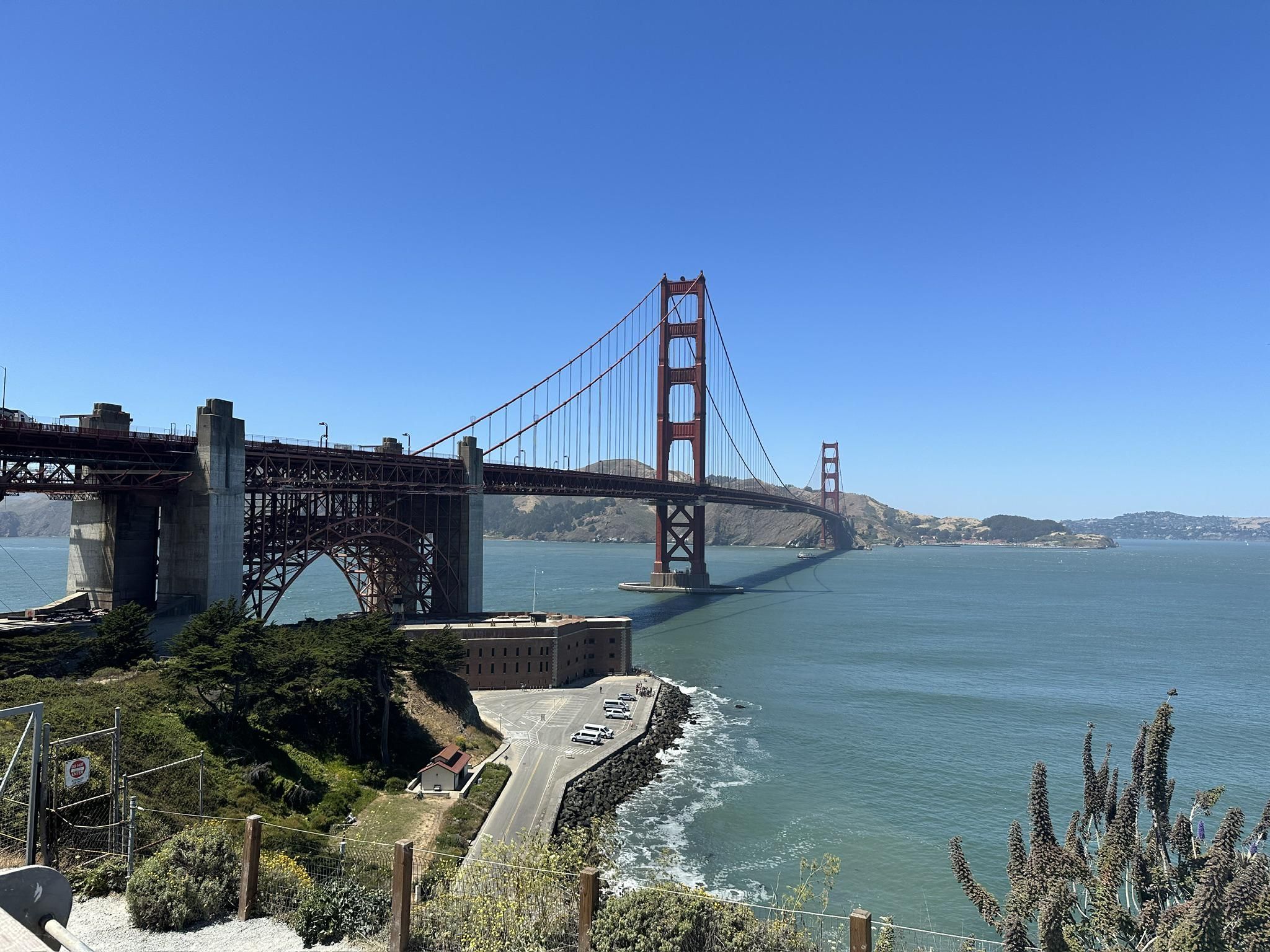 Large red suspension bridge over water, with a building and road. - Across the Golden Gate Bridge to Sausalito