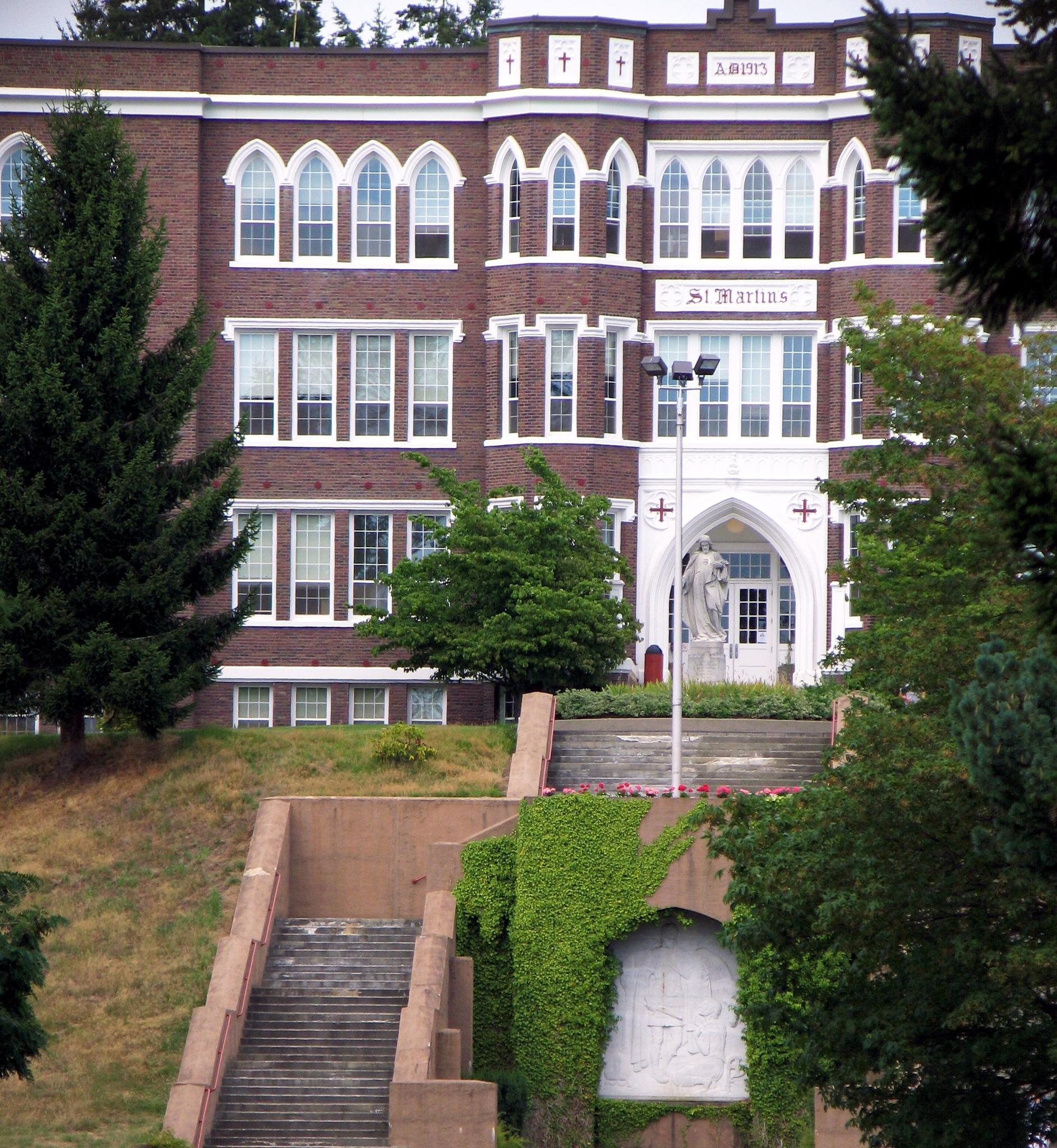 Large brick building with arched entrance, statue, and grand stairs under daylight.