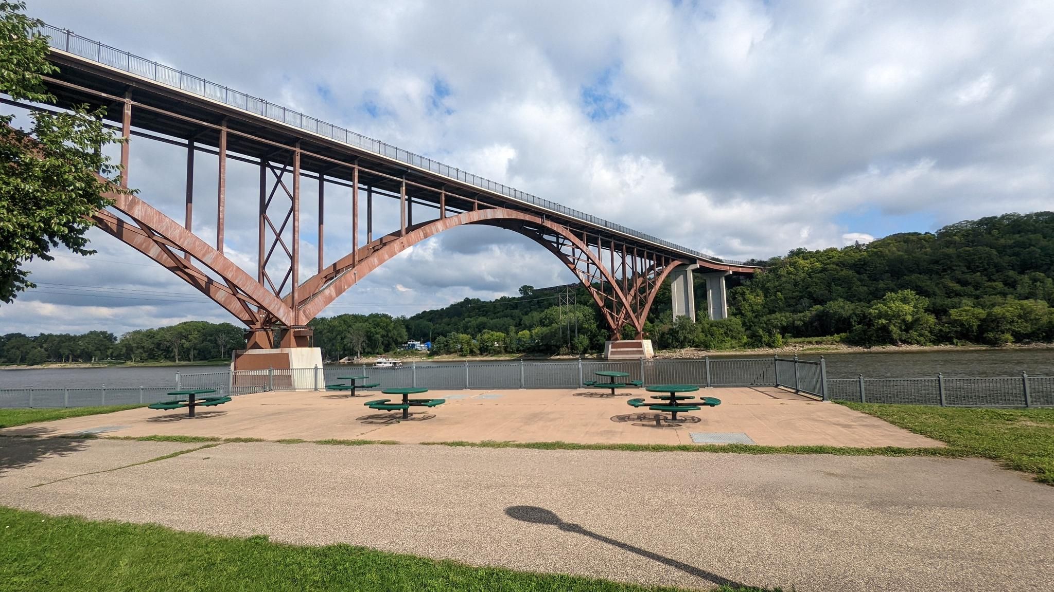 Large arched bridge over a river with picnic tables under cloudy sky. - St. Paul - Mississippi River Trail Loop