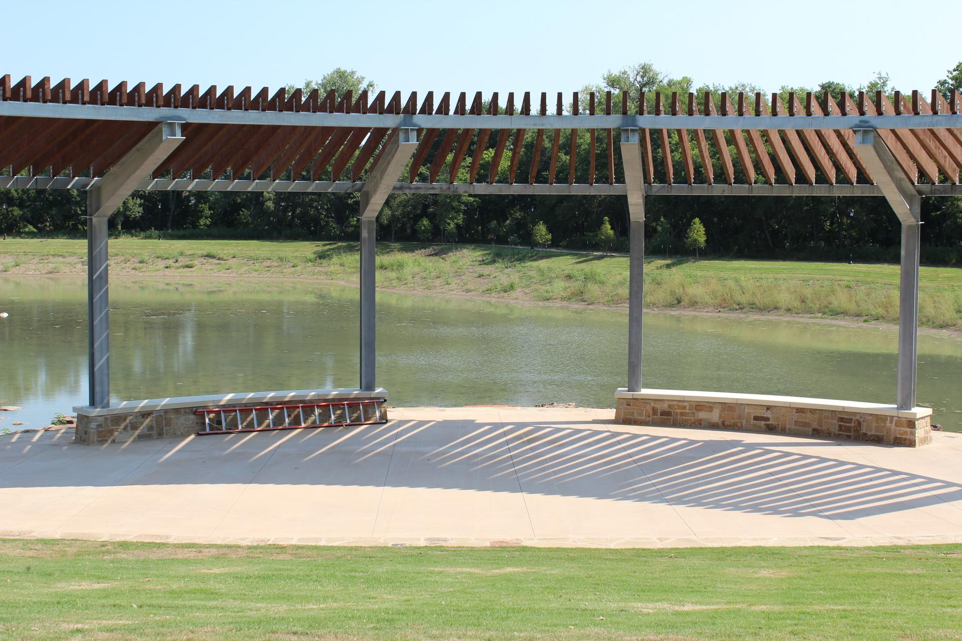 Modern pergola with benches overlooks a calm lake on a sunny day.