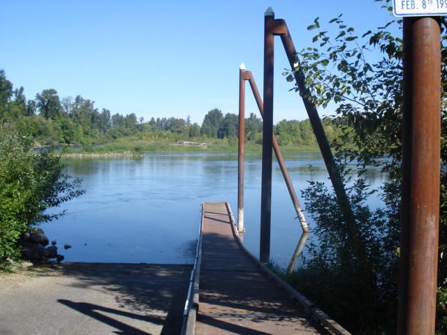 Sunny view of a boat ramp leading to a calm river with distant trees.