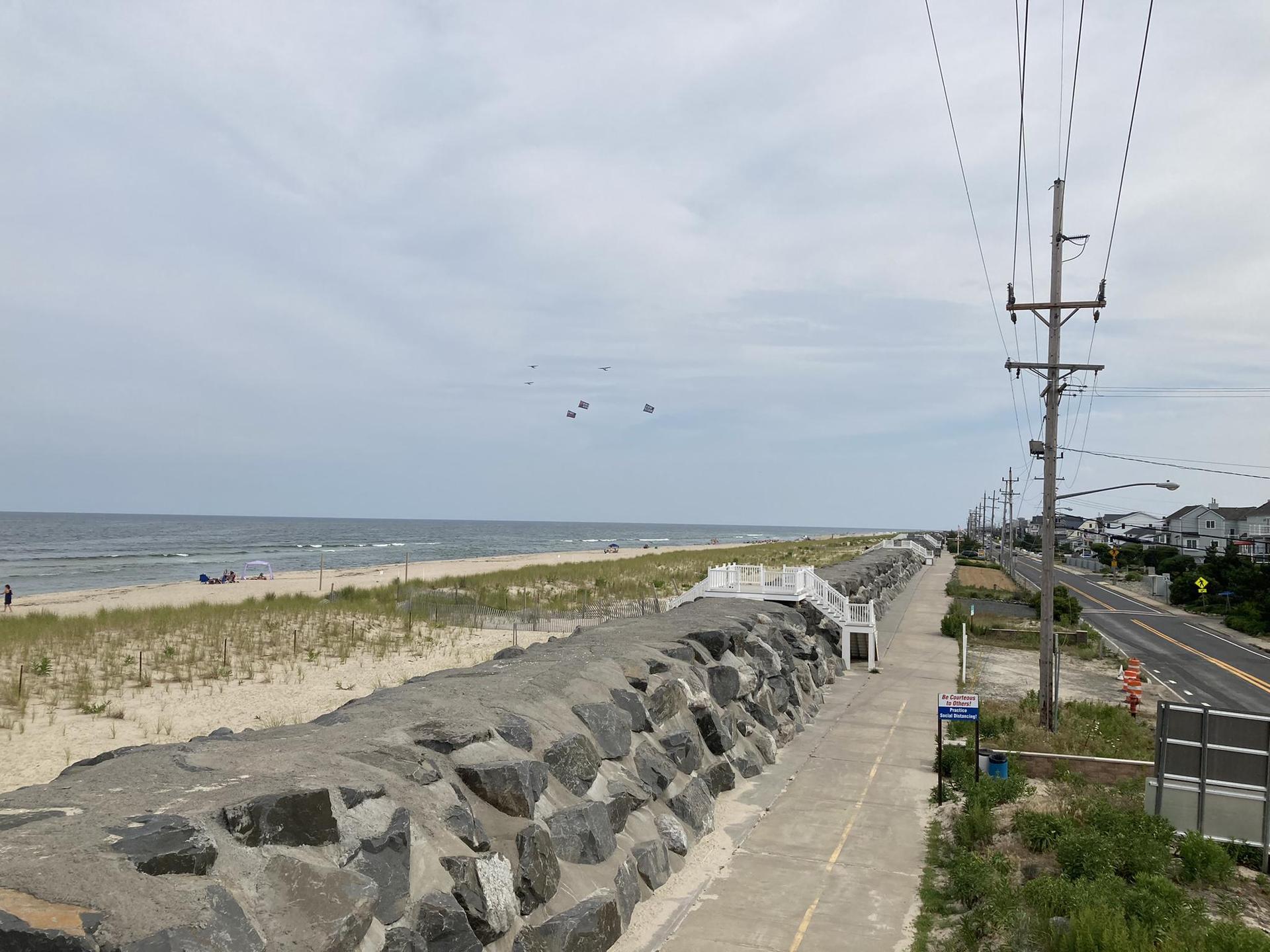 Overcast day at a beach with a rock wall, road, and distant people.