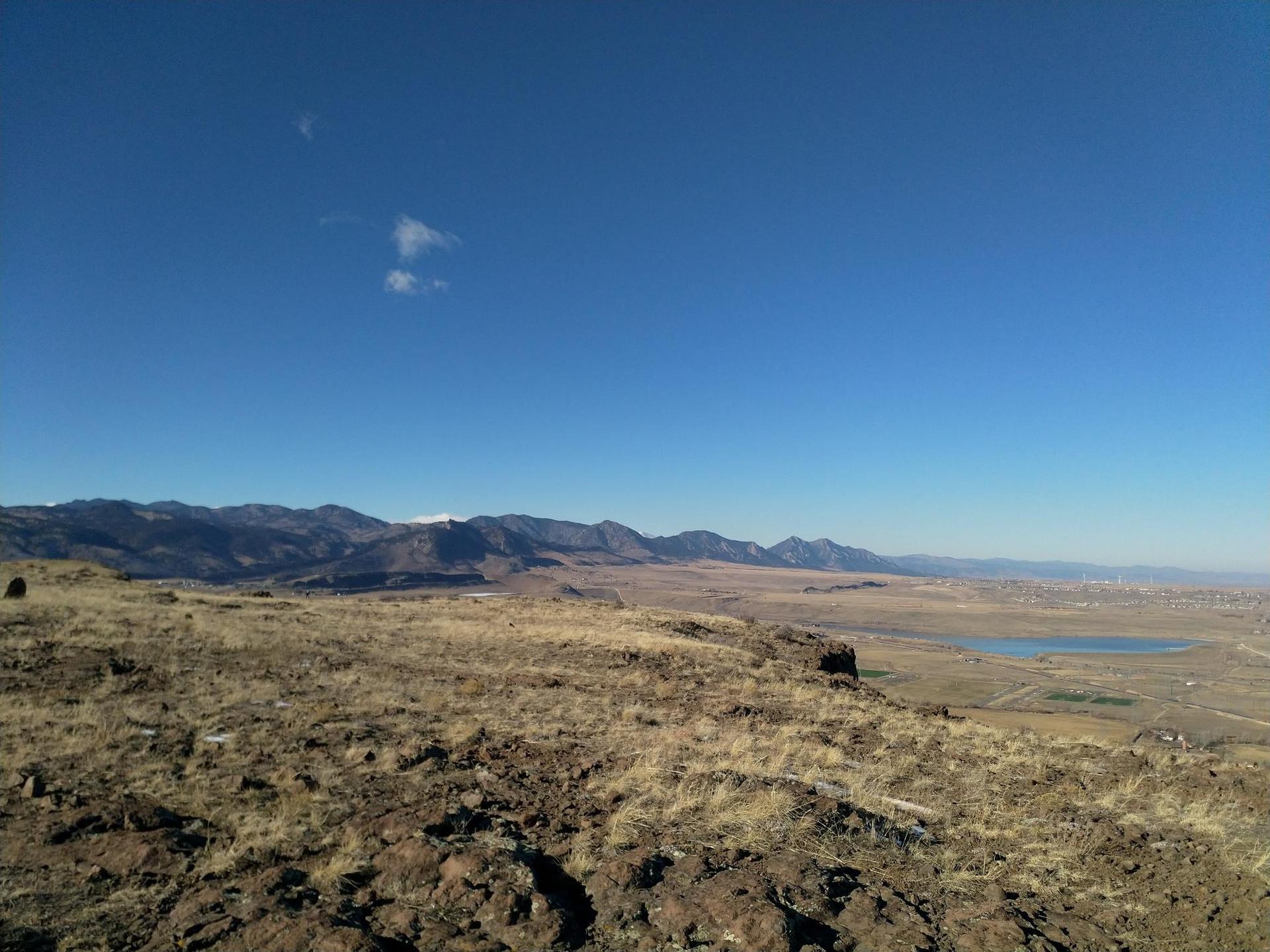 Sunny panoramic view of dry plains, distant mountains, and a lake.