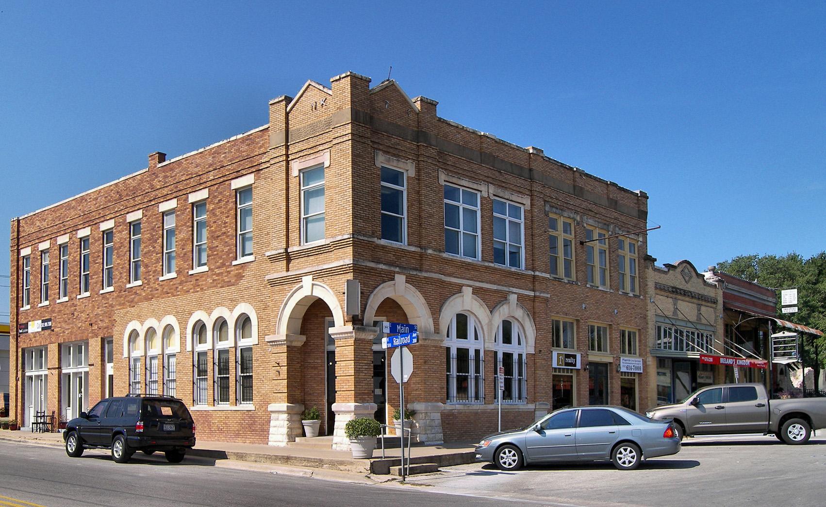 Historic brick building with arched windows on a sunny street corner.