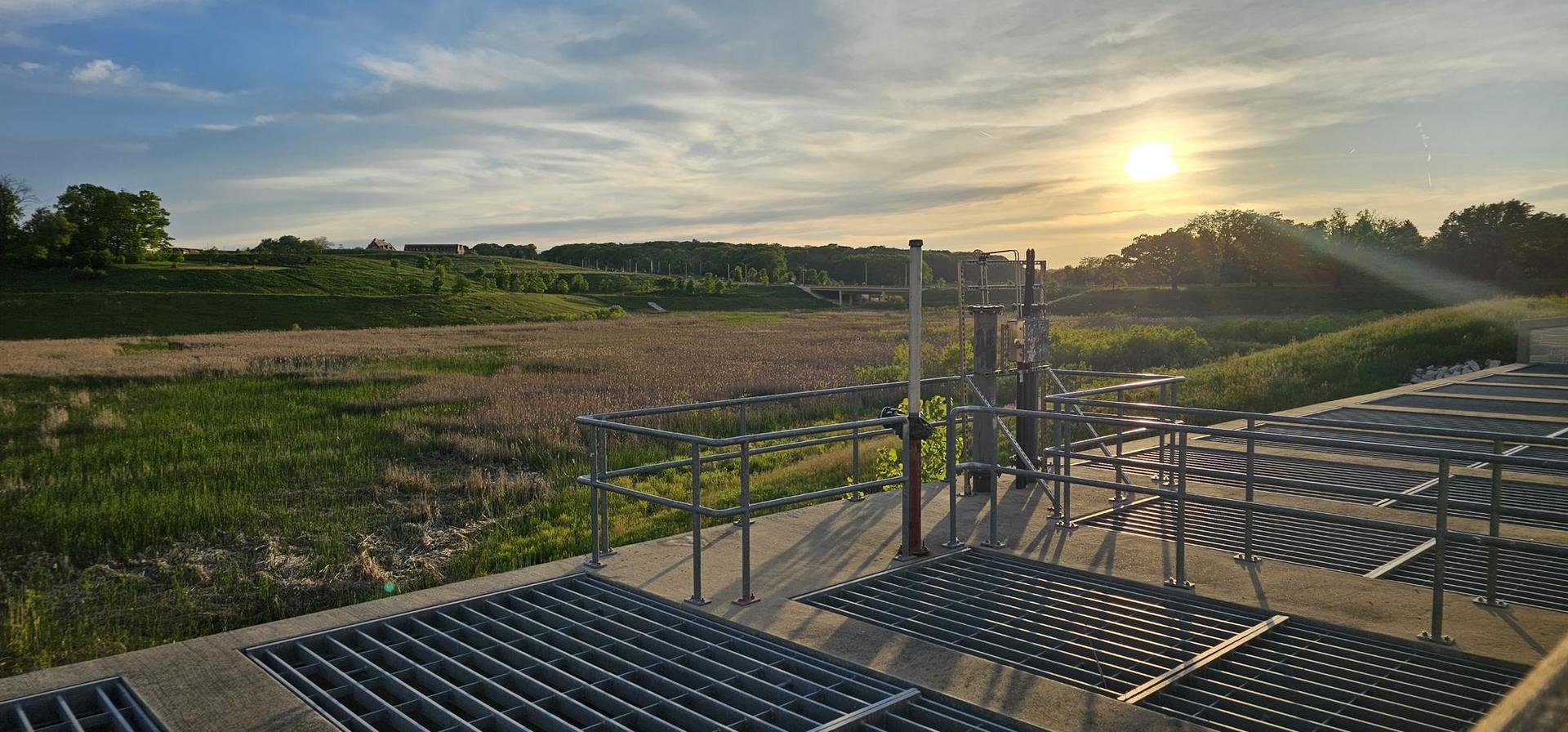 Industrial structure overlooking a vast field at sunset, casting long shadows.