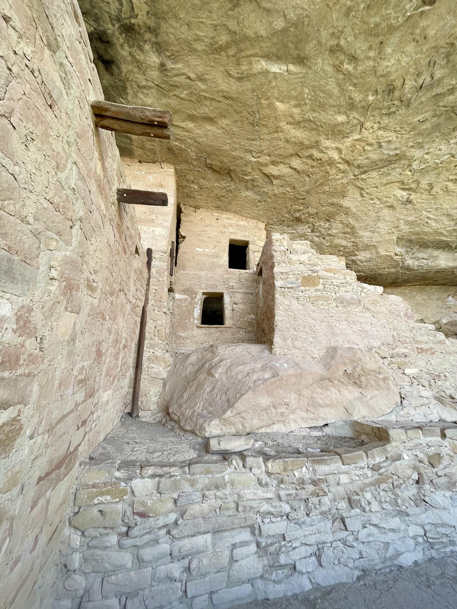 Ancient stone dwelling built into a rock overhang, illuminated by daylight.