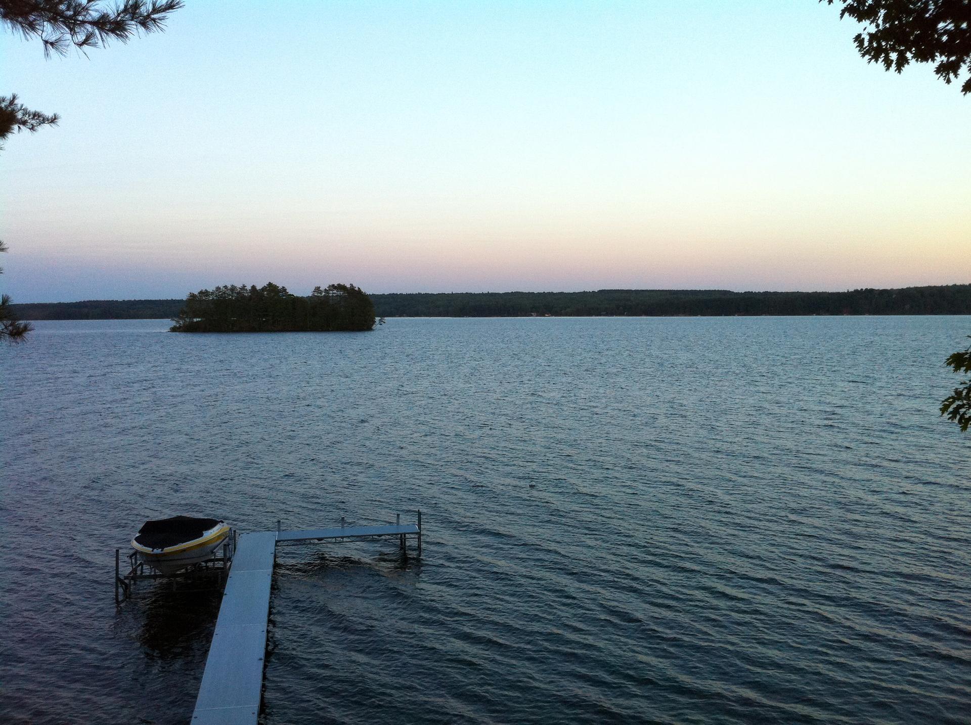 Calm lake at dusk with a dock, boat, and distant island.