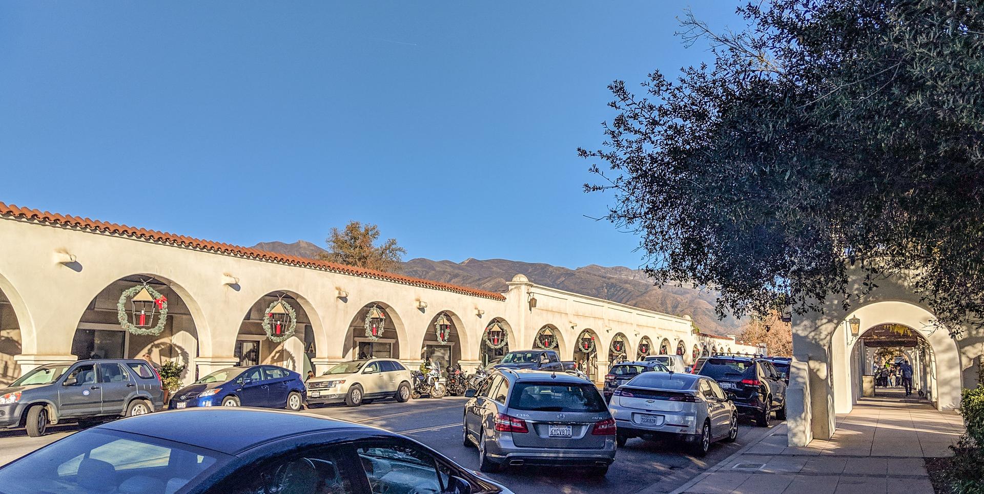 Arched building with holiday decorations, street with cars, and distant mountains on a sunny day.