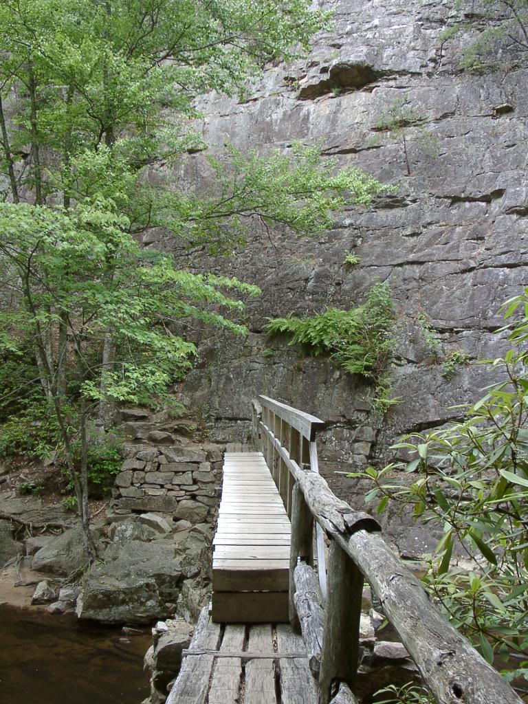 A wooden footbridge leads towards a tall, rocky cliff face.