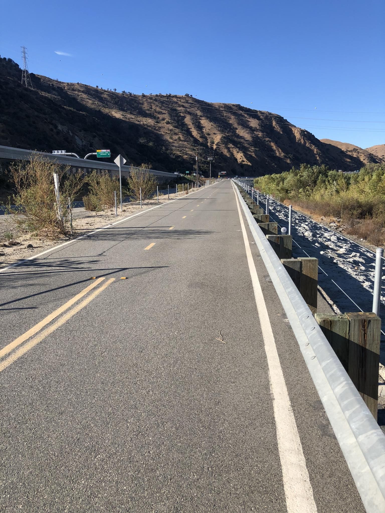 A long paved path with guardrails alongside a dry, sunny mountainside. - Bike loop from Fantasy Burger