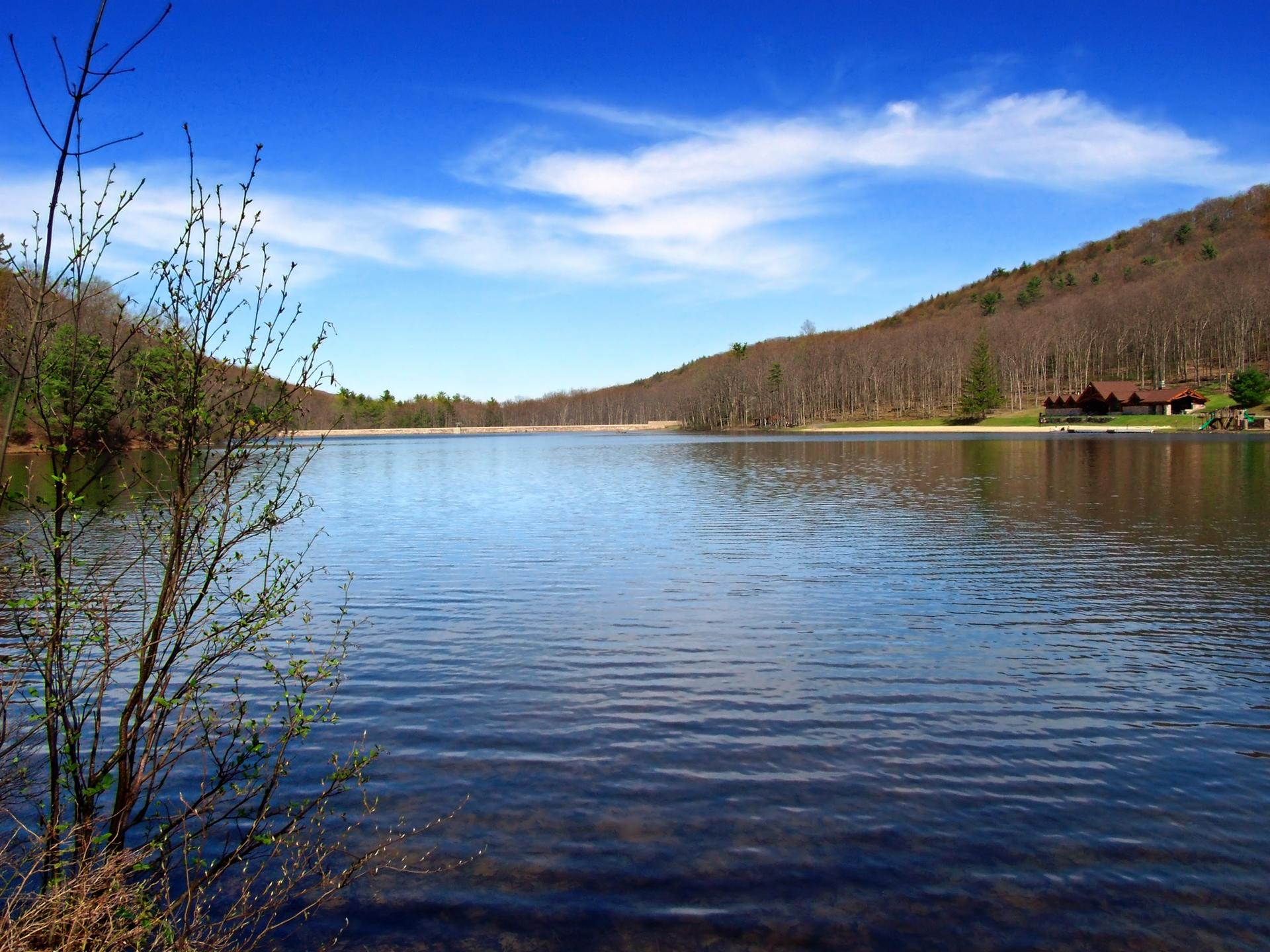 Calm lake reflecting a bright blue sky, surrounded by wooded hills.
