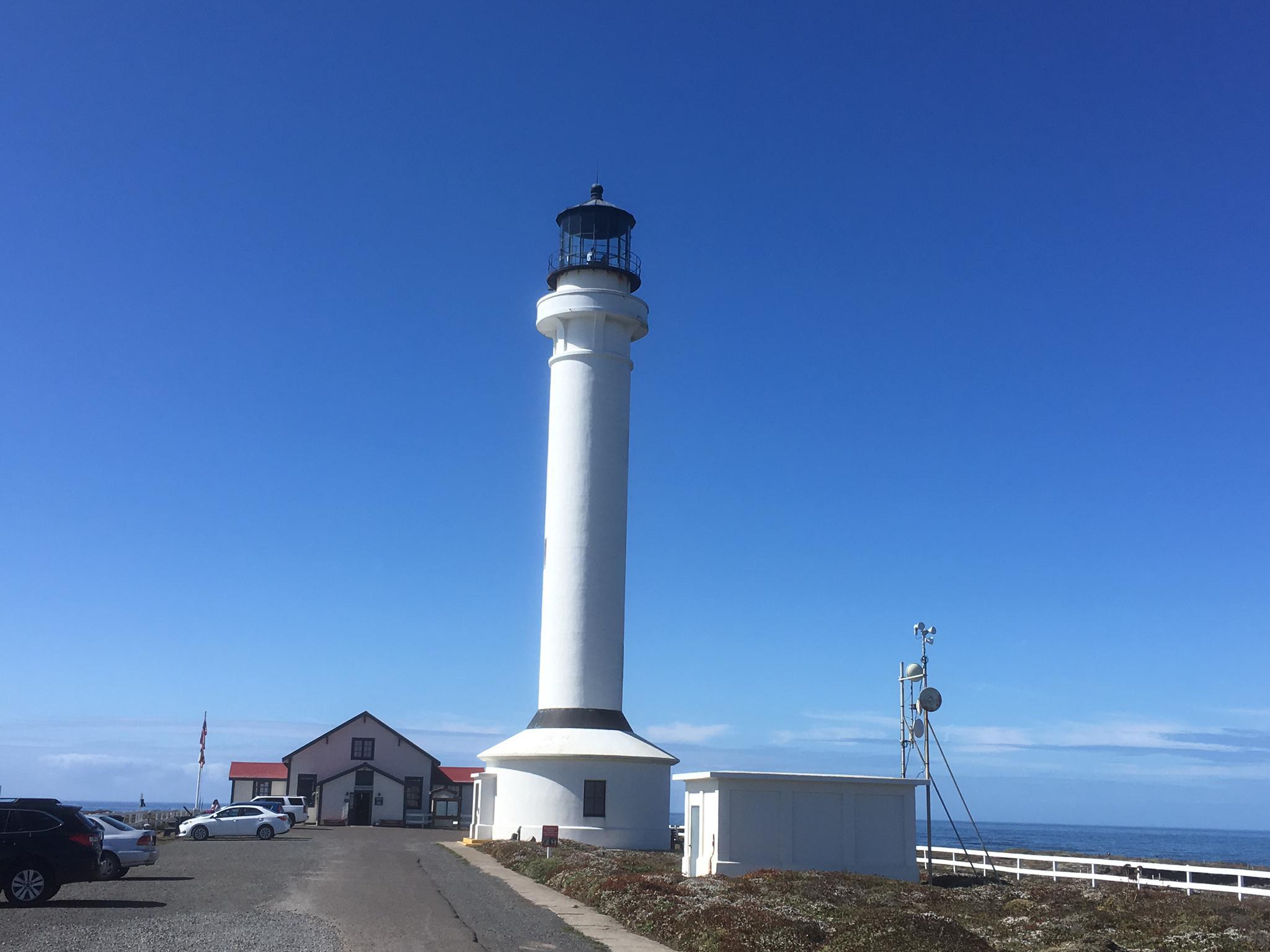A tall white lighthouse stands under a clear blue sky by the ocean.