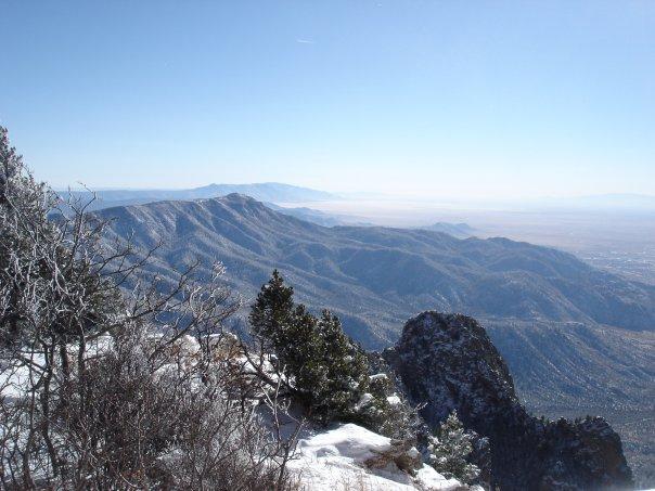 Snow-dusted mountain peaks and trees overlooking a vast, hazy valley.