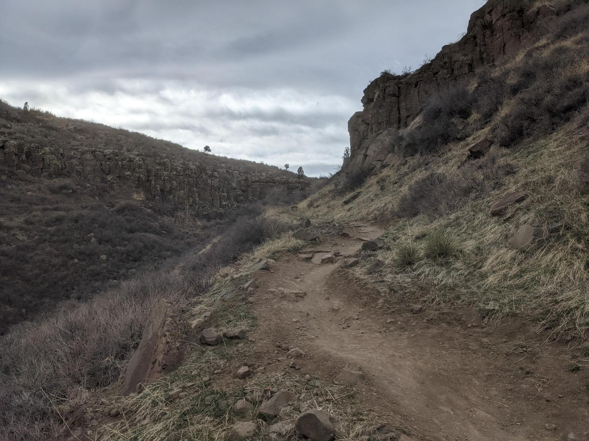 Winding dirt trail through a rocky canyon under an overcast sky.
