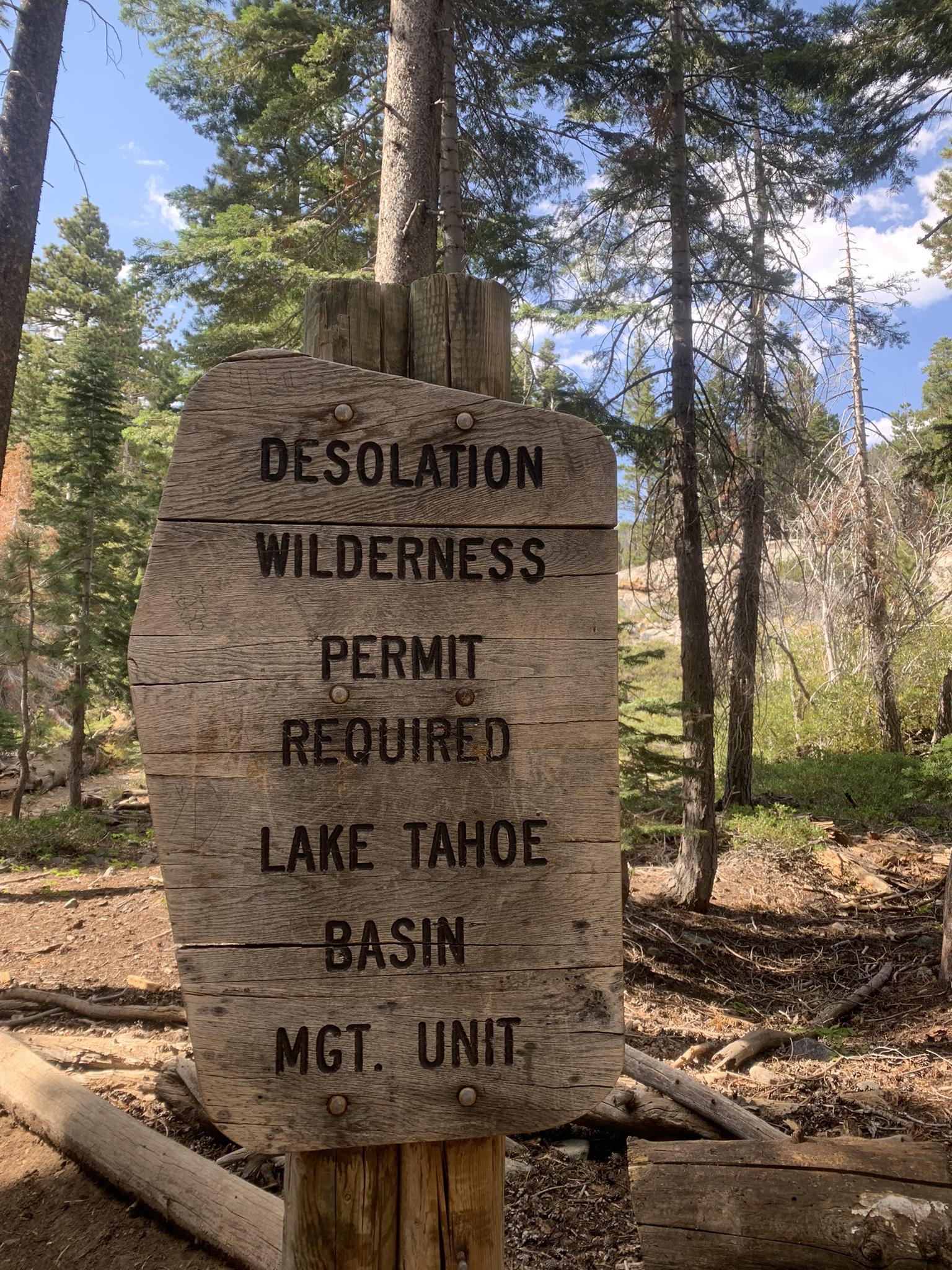 A rustic wooden sign in a forest indicating permit requirements.